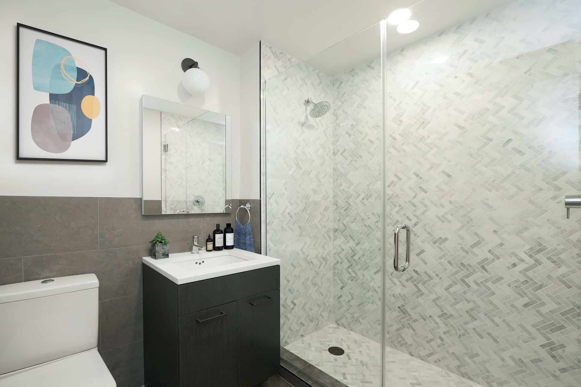 Bathroom at 101 East 10th Street with single vanity, square mirror, and a standing shower with herringbone tile pattern.