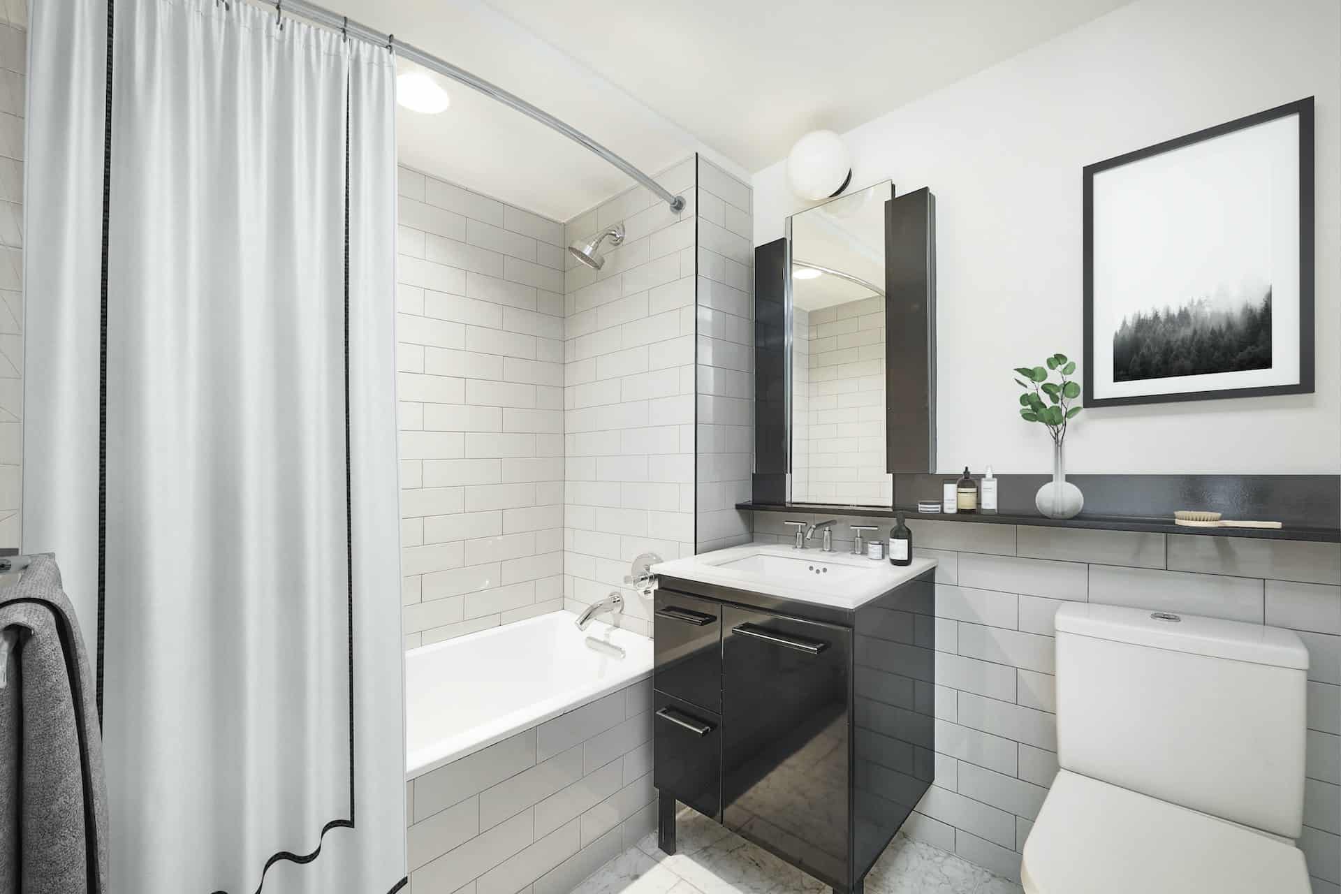 Bathroom at 101 East 10th Street with single vanity, vertical rectangle mirror, and a soaking tub with shower and white tile.