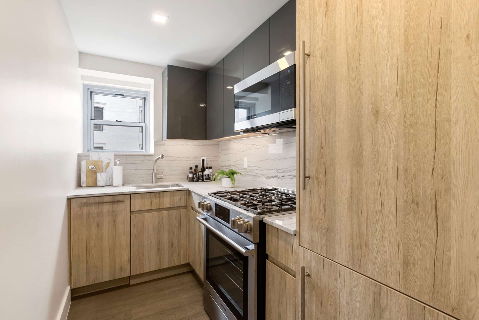 Enclosed kitchen with white stone countertops, stainless steel range & grey upper cabinets at 60 East 12th Street apartments.