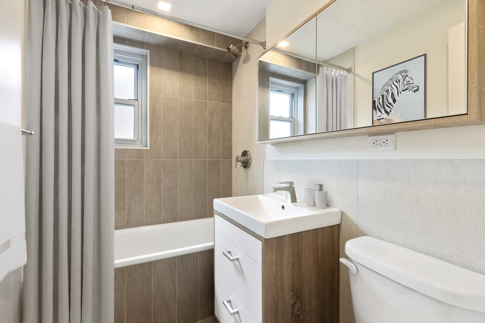 Bathroom at 60 East 12th Street apartment with single vanity, large rectangle mirror cabinet and soaking tub with shower.