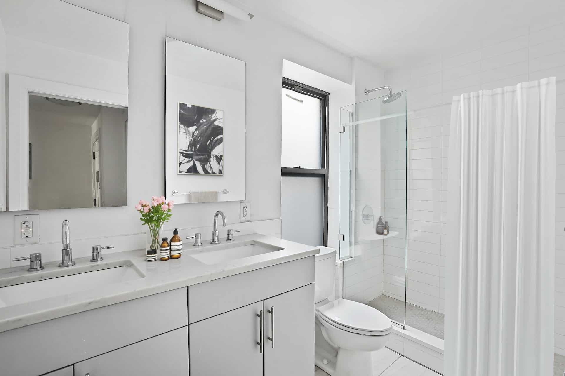 Bathroom at 556-566 West 126th Street apartments in New York with a double vanity, two square mirrors and a walk-in shower.