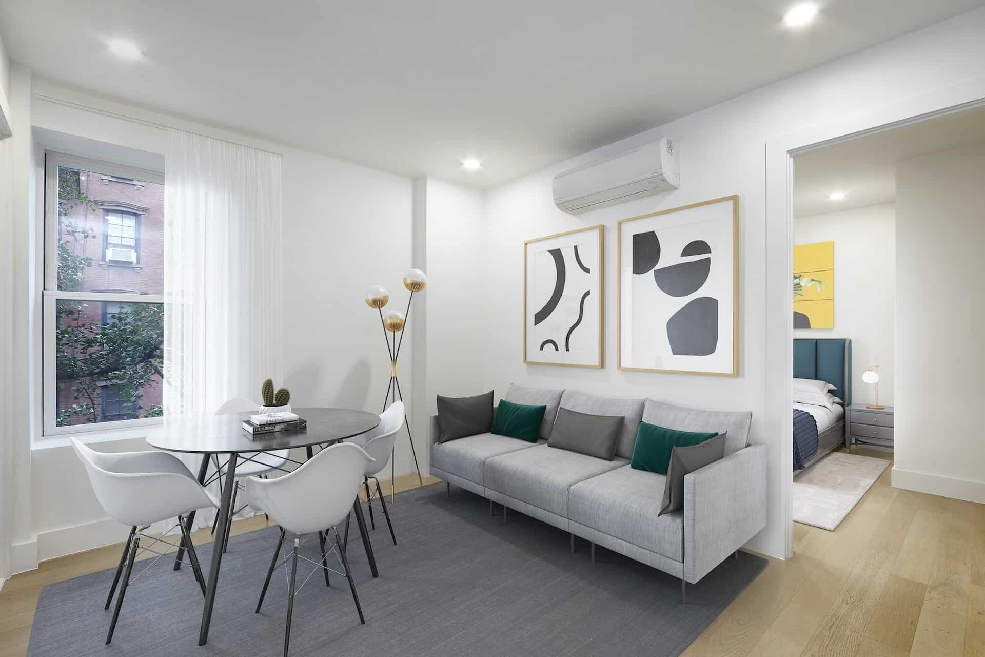 Living room at 236 West 10th Street apartments with a couch, round table, windows, hardwood floors and a bedroom door.