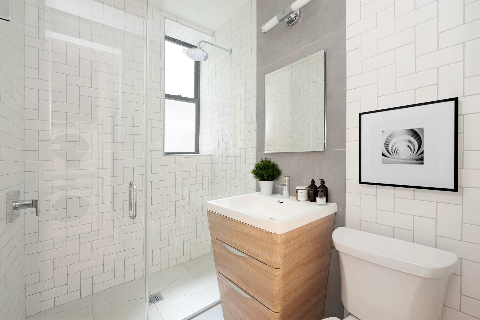 Bathroom at 244 East 7th Street apartments in New York. White tile walls, single vanity with square mirror & walk-in shower.