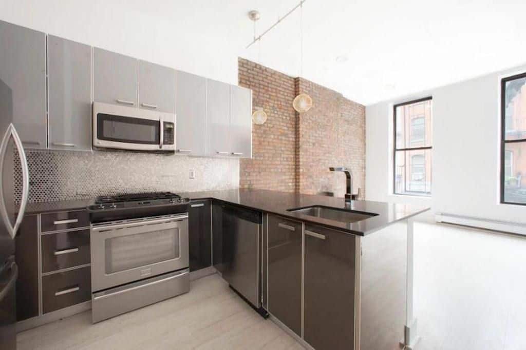 Kitchen at 324 Bowery Street apartments with black stone countertops, stainless steel appliances and hardwood floors.