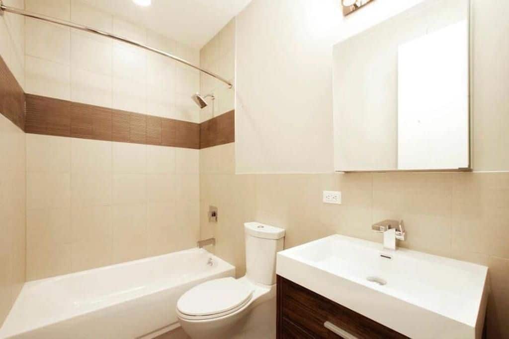 Bathroom at 324 Bowery Street apartments with a single vanity, square mirror, tile walls and soaking tub with a shower.