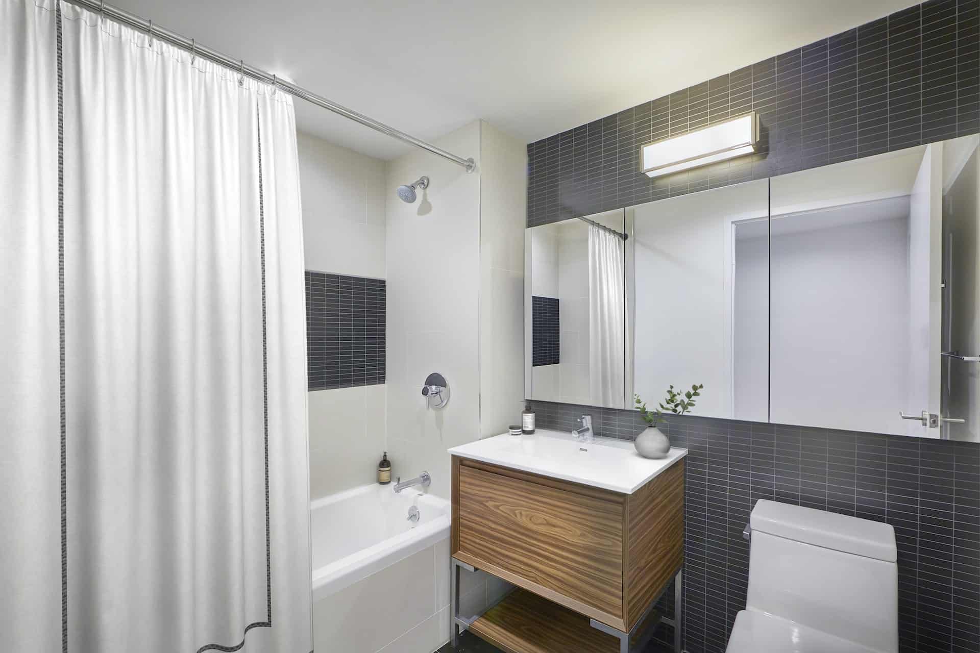 Bathroom at 325 Lafayette Avenue apartments in Brooklyn with single vanity, a large mirror and a soaking tub with shower.