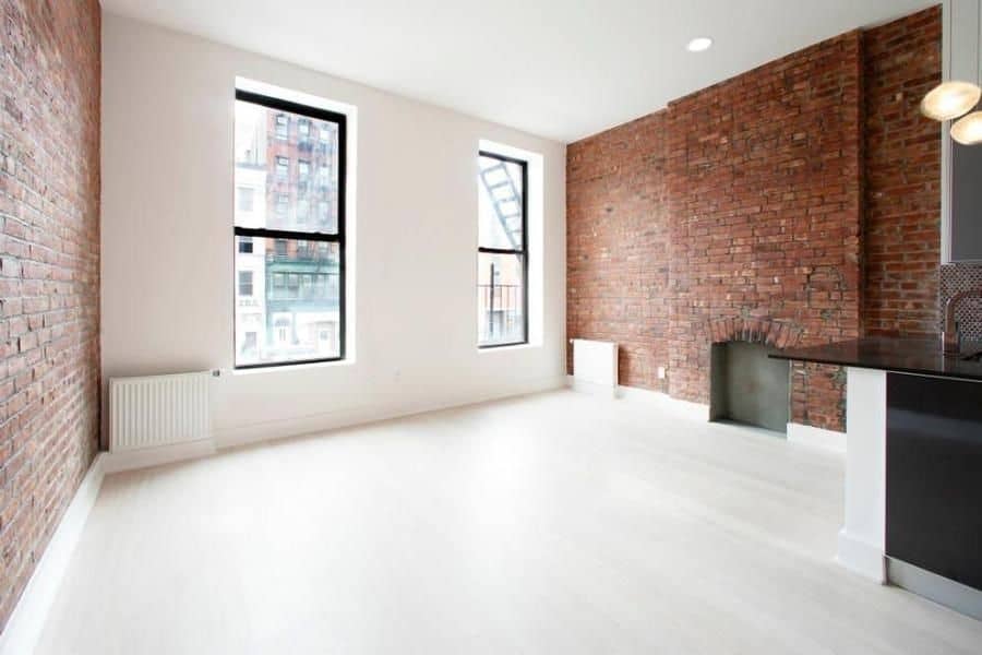 Living room at 324 Bowery Street apartments with tall windows, hardwood floors, and brick accent wall with a fireplace.