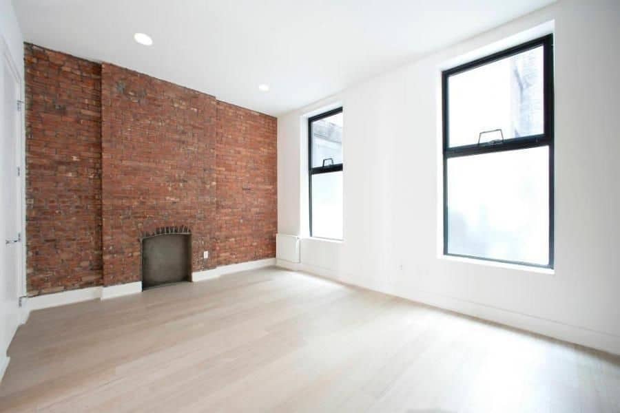 Living room at 324 Bowery Street apartments with 2 tall windows, hardwood floors, and brick accent wall with a fireplace.
