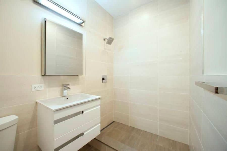 Bathroom at 324 Bowery Street apartments with a single vanity, square mirror, white tile walls and a walk-in shower.