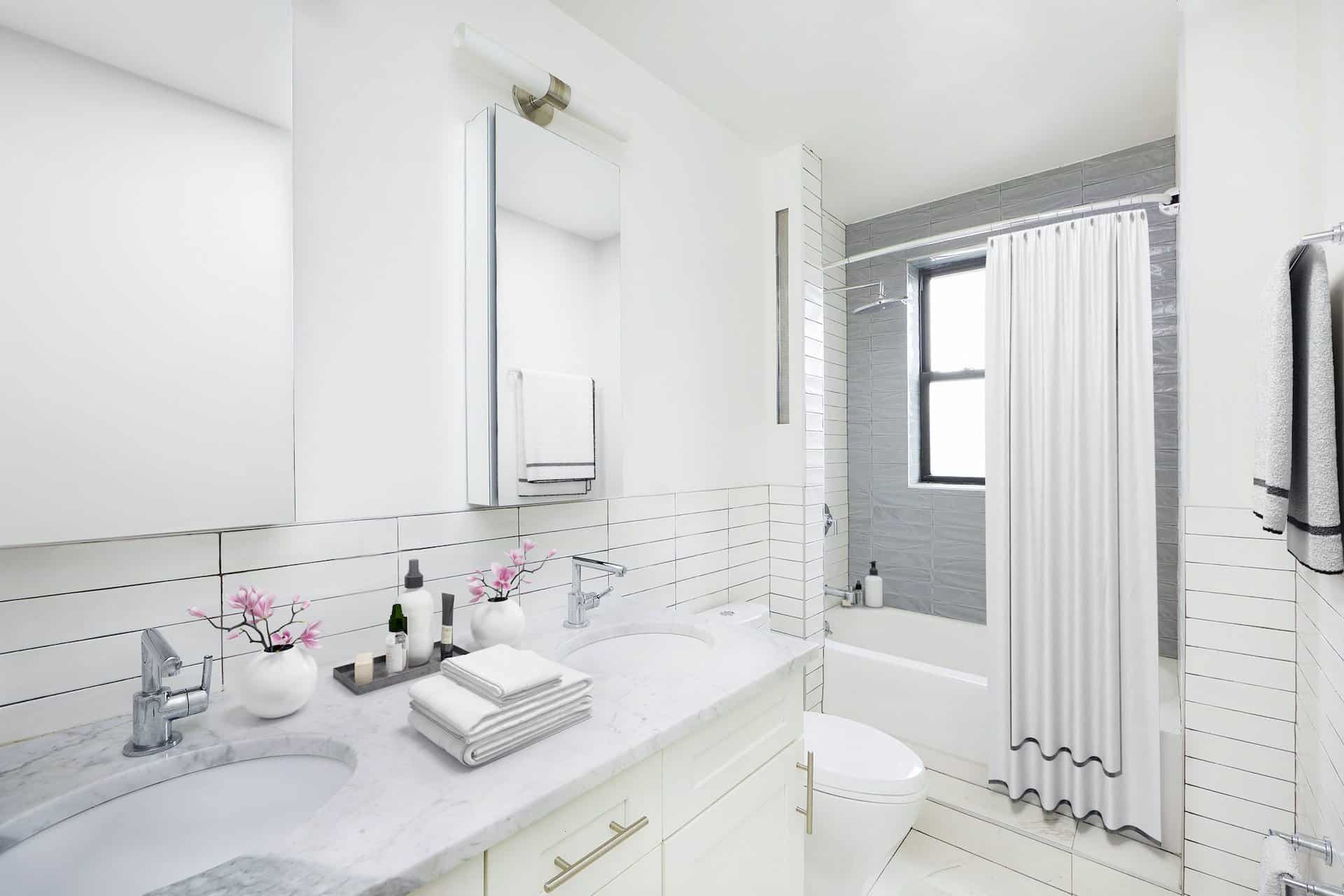 Bathroom at 457 15th Street apartments with a double vanity, mirrors, subway tile on the walls and a soaking tub with shower.