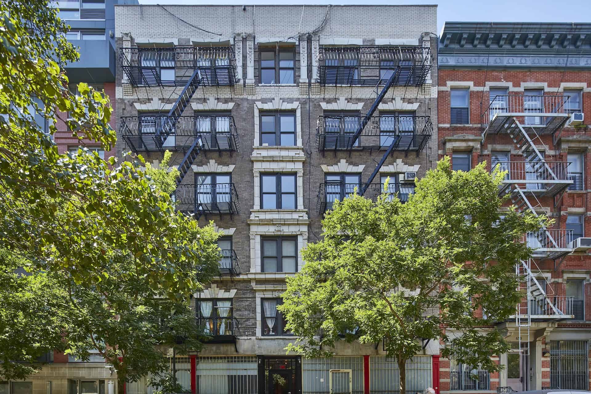 Street view of 634 East 11th Street, a brick apartment building in New York with front fire escapes and trees out front.