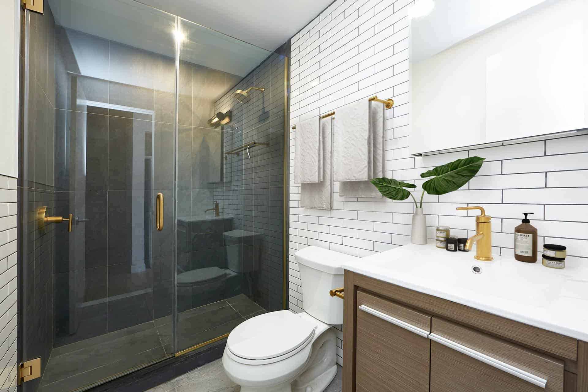 Bathroom at 634 East 11th Street apartments in New York. Tile walls, single vanity with rectangle mirror and walk-in shower.