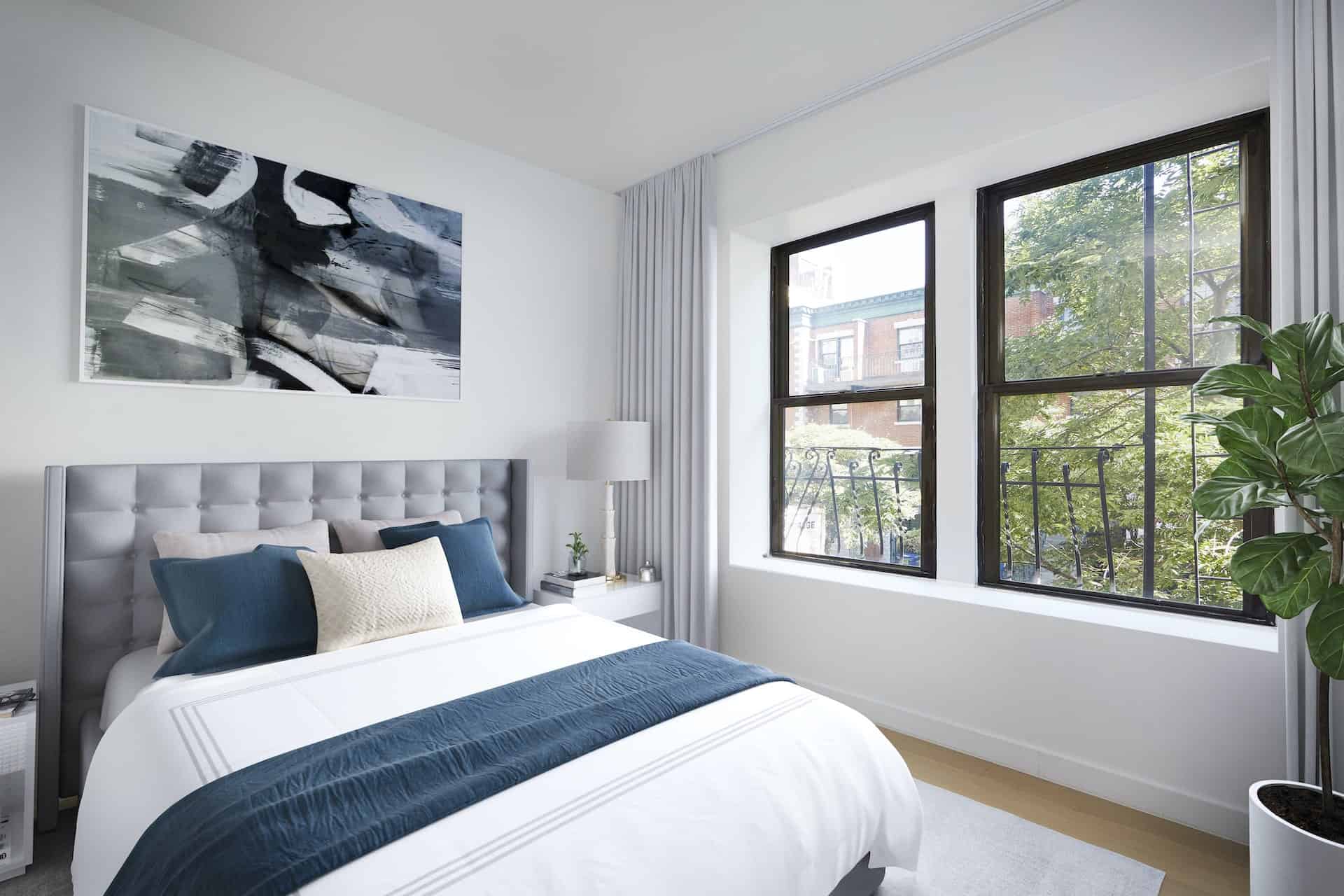 Bedroom at 634 East 11th Street apartments in New York. Queen bed with headboard, matching side tables and large windows.