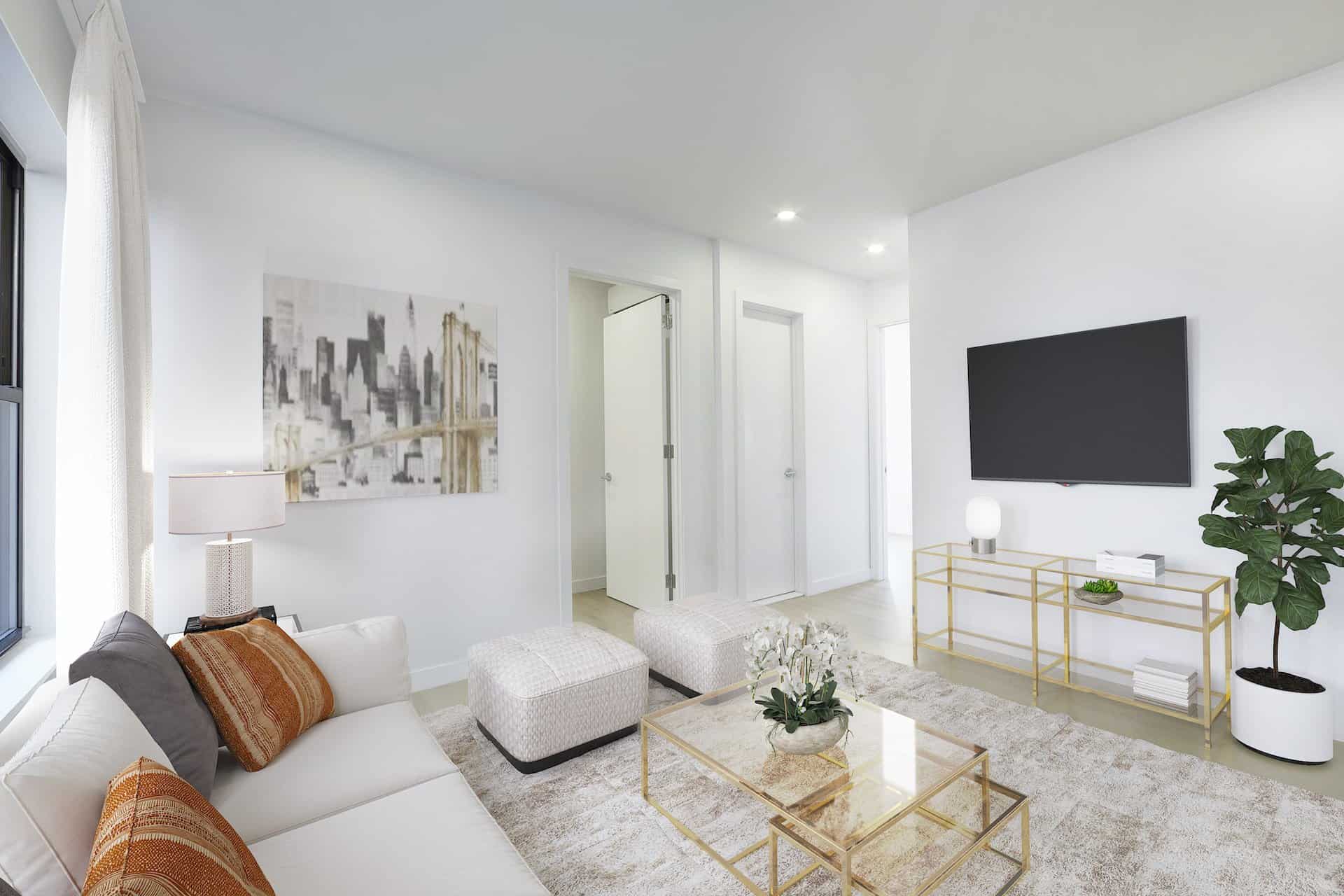 Living room at 634 East 11th Street apartments in New York. A white couch, glass coffee table, hardwood floors & mounted tv.