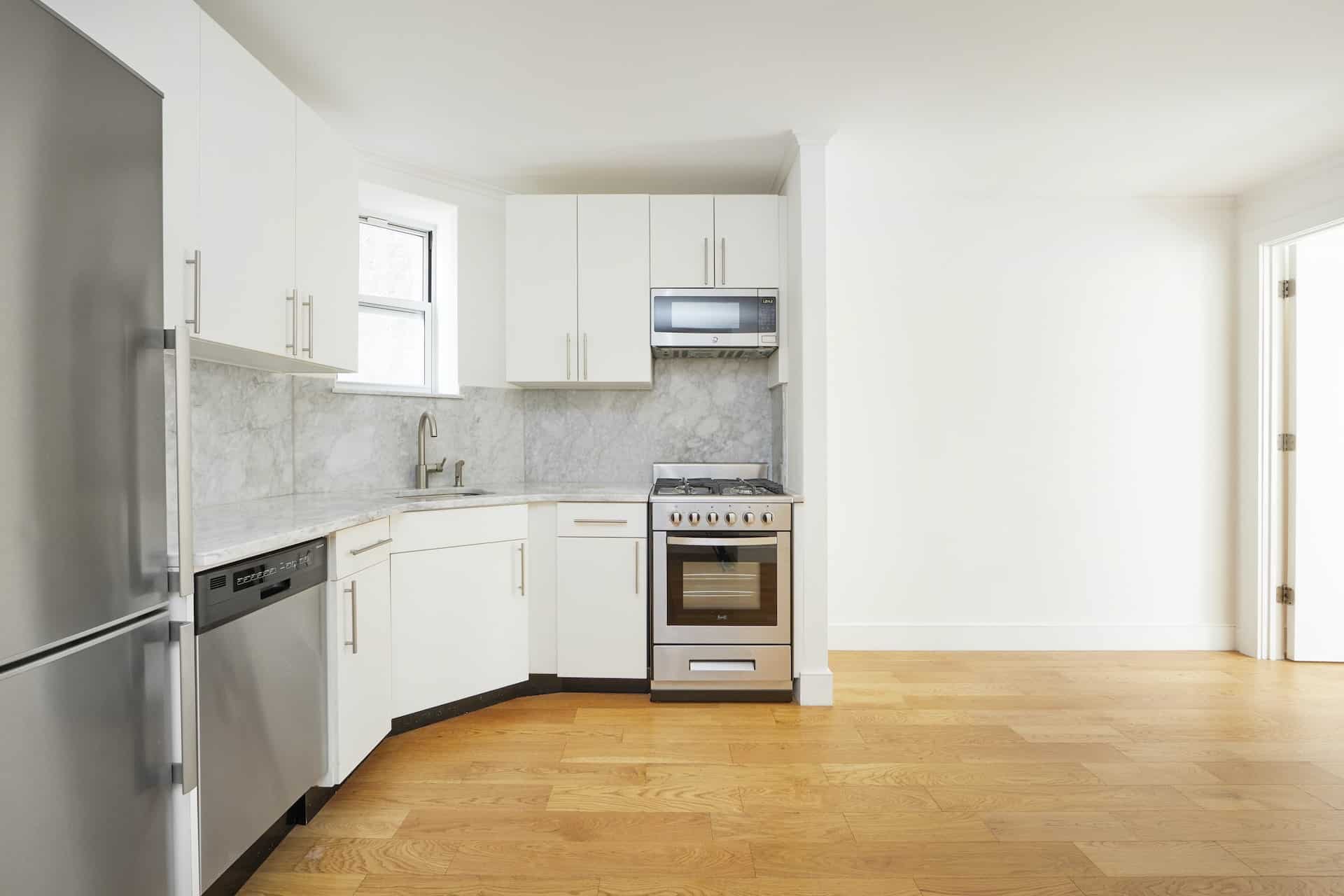 Kitchen at 207 East 33rd Street apartments with stone countertops, white cabinets, stainless steel appliances & hardwoods.