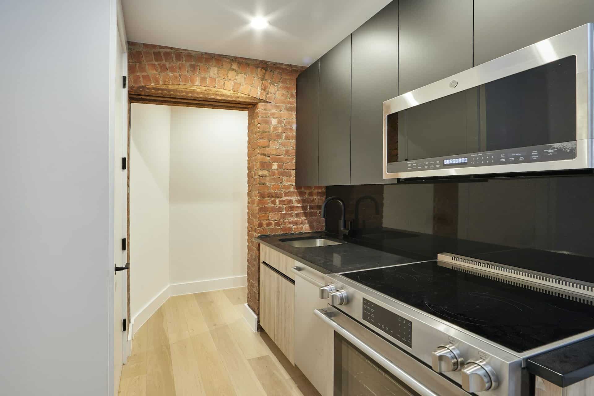 Kitchen at 207 East 33rd Street apartments with dark grey countertops, stainless steel appliances and hardwood floors.