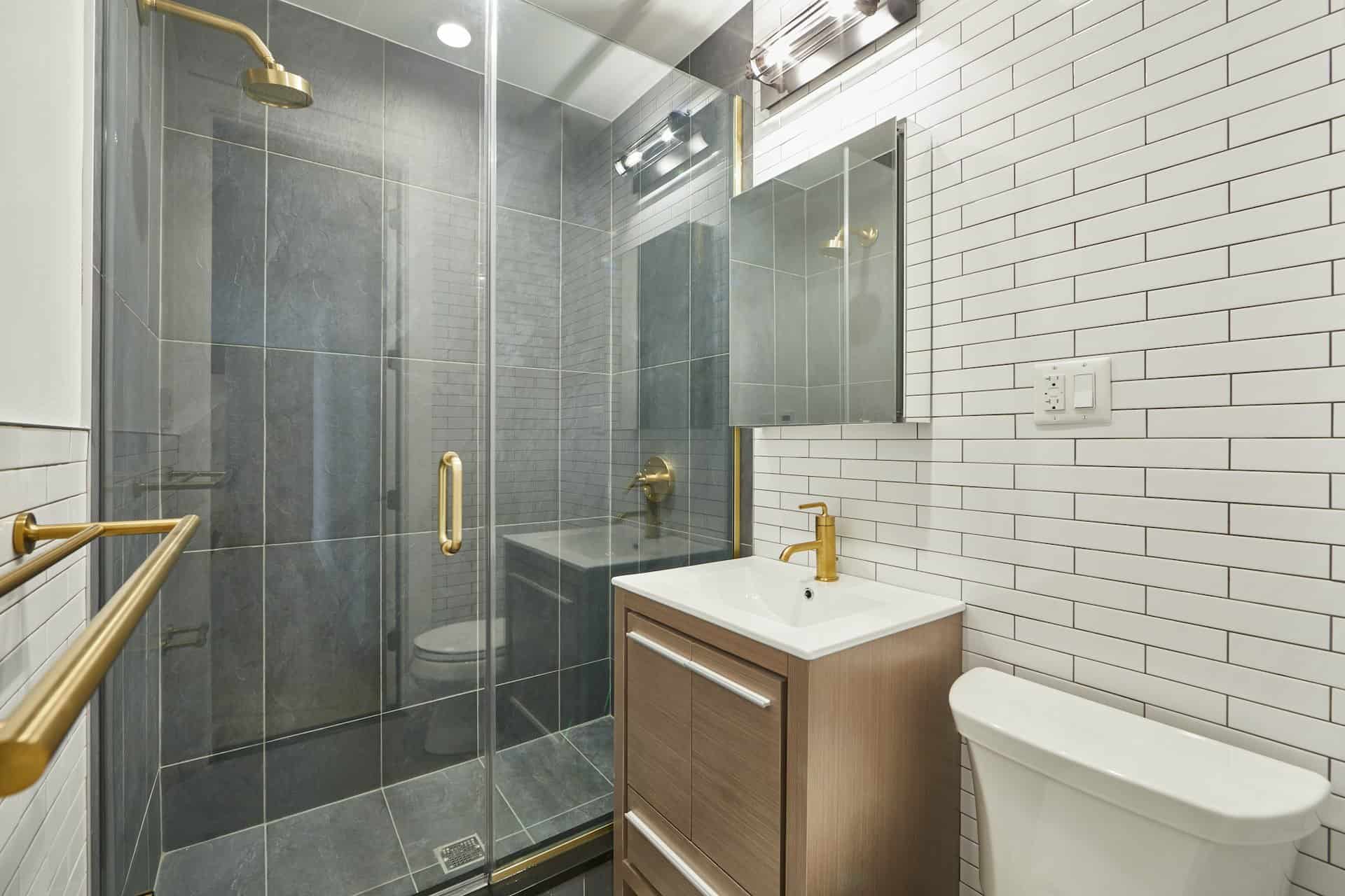Bathroom at 207 East 33rd Street apartments with tile walls, single vanity, a square mirror cabinet and walk-in shower.