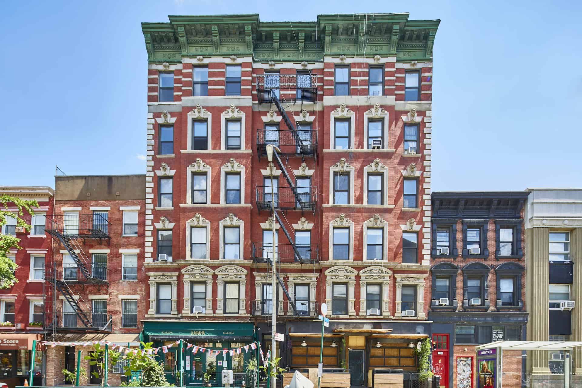 Street view of 112-116 Avenue C apartments in New York. Tall red brick building with white bricks bordering the windows.