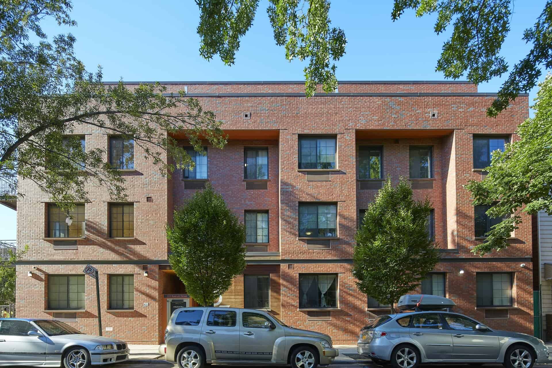 Exterior of 83 Bushwick Place apartments in Brooklyn. Brick residential building with trees and cars parked on the street.