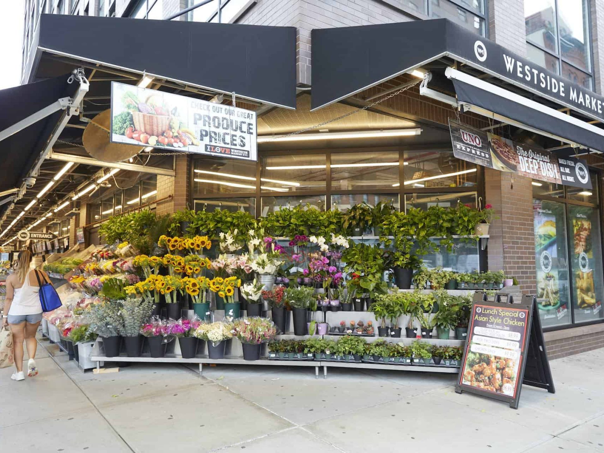 Flower display on the sidewalk outside of Westside Market in Brooklyn. Tiered flower display, hanging banners and an A-board.