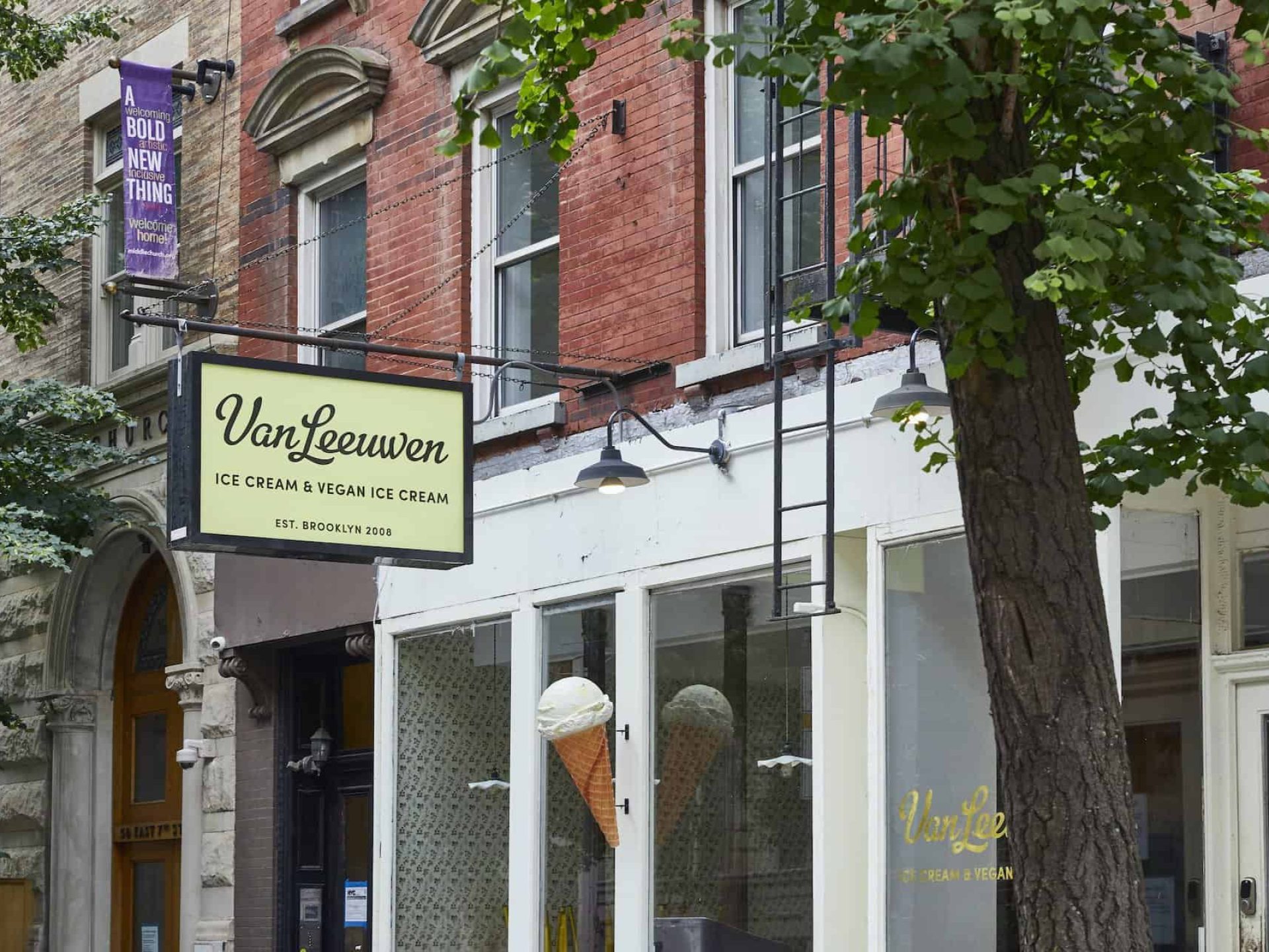 Street view of Van Leeuwen Ice Cream & Vegan Ice Cream shop in Brooklyn. Elevated store sign above large windows with decals.