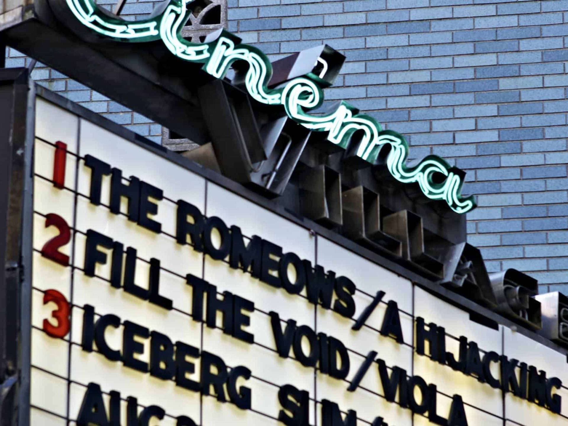 Close up of Cinema Village Theater sign displaying indie-films currently showing with brick wall in the background.