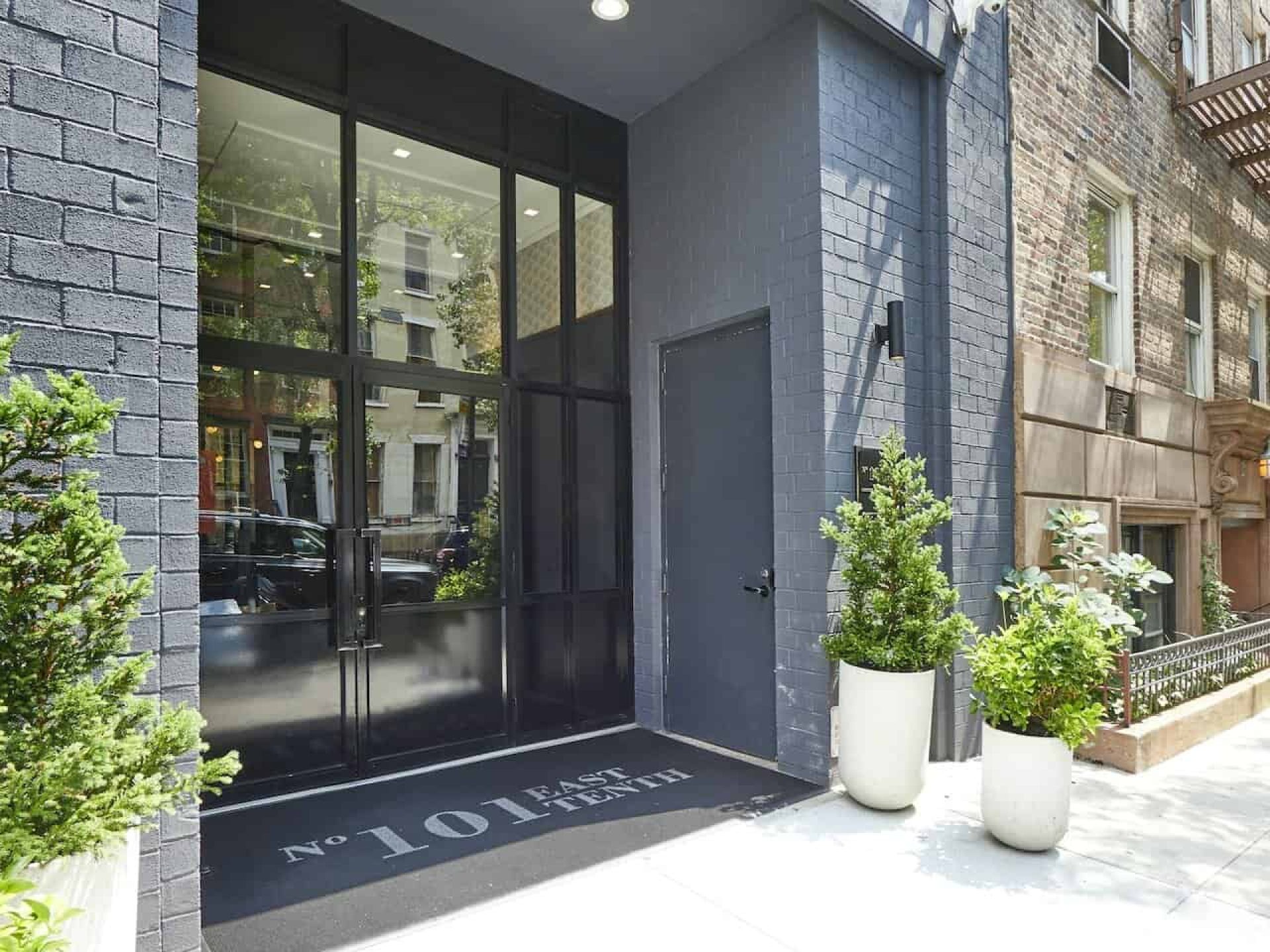 Entrance to 101 East 10th Street luxury apartments. Tall glass double doors under stone overhang with potted plants.