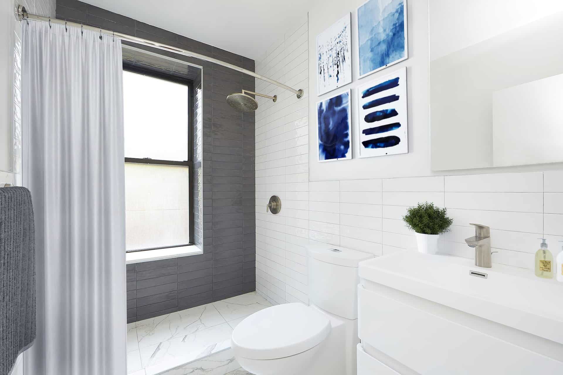 Bathroom at 112-116 Avenue C apartments in New York with white tile walls, single vanity, standing shower and a large window.