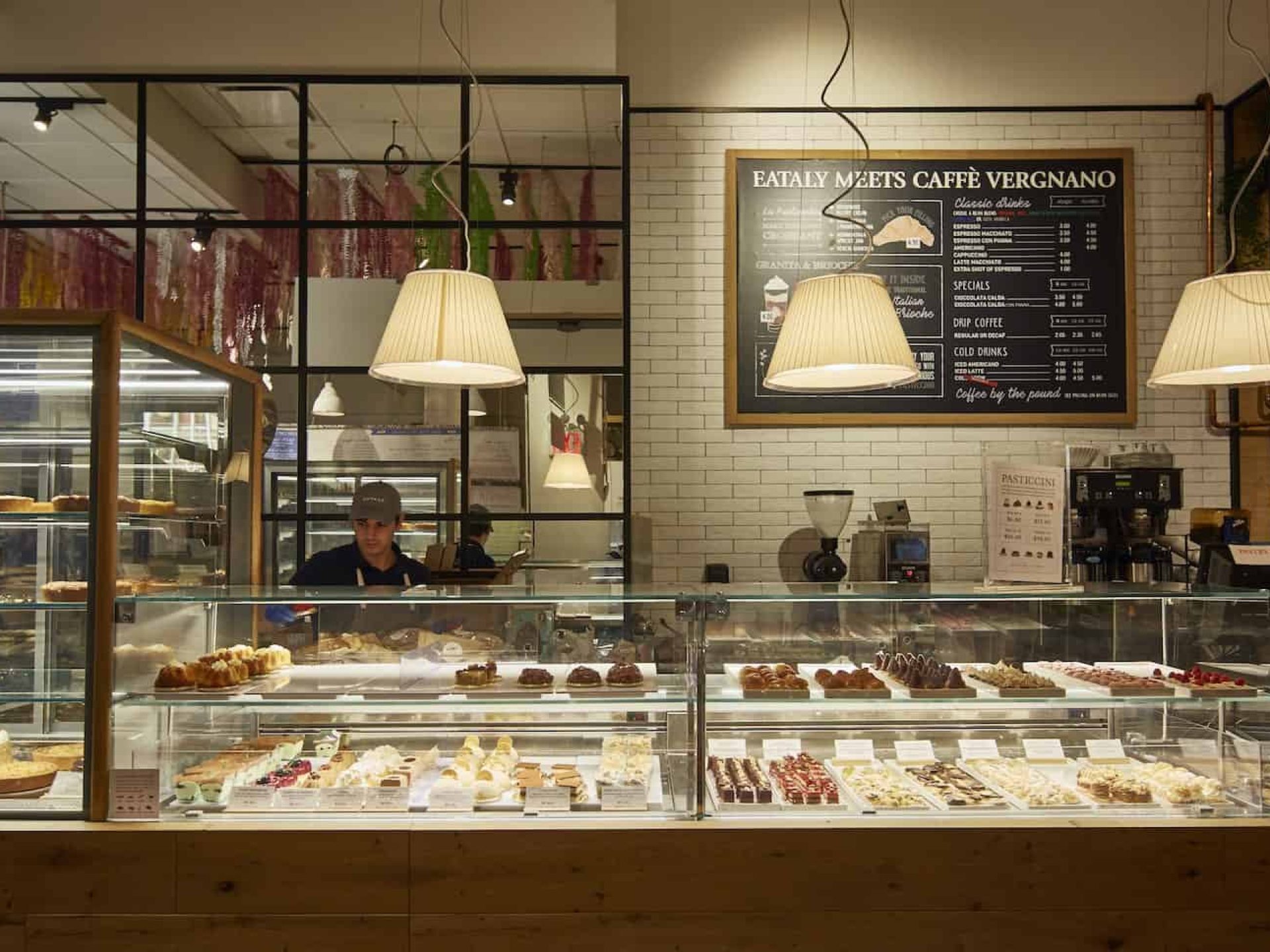 Glass display case filled with pastries and counter in Eataly Market with coffee makers and employees in the background.
