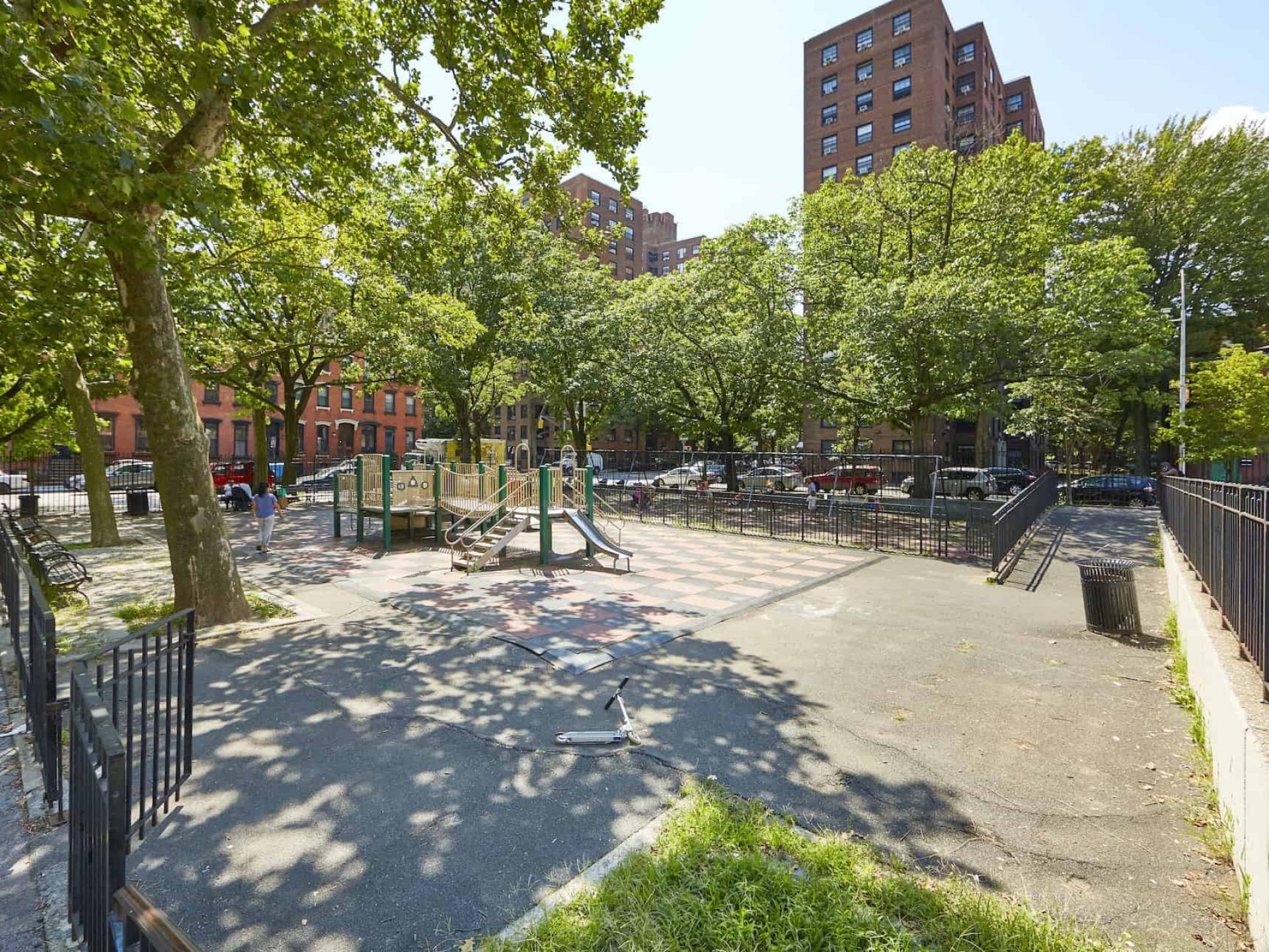 City park and playground in New York City with play set on a checkered rubber mat and swing sets in the background.