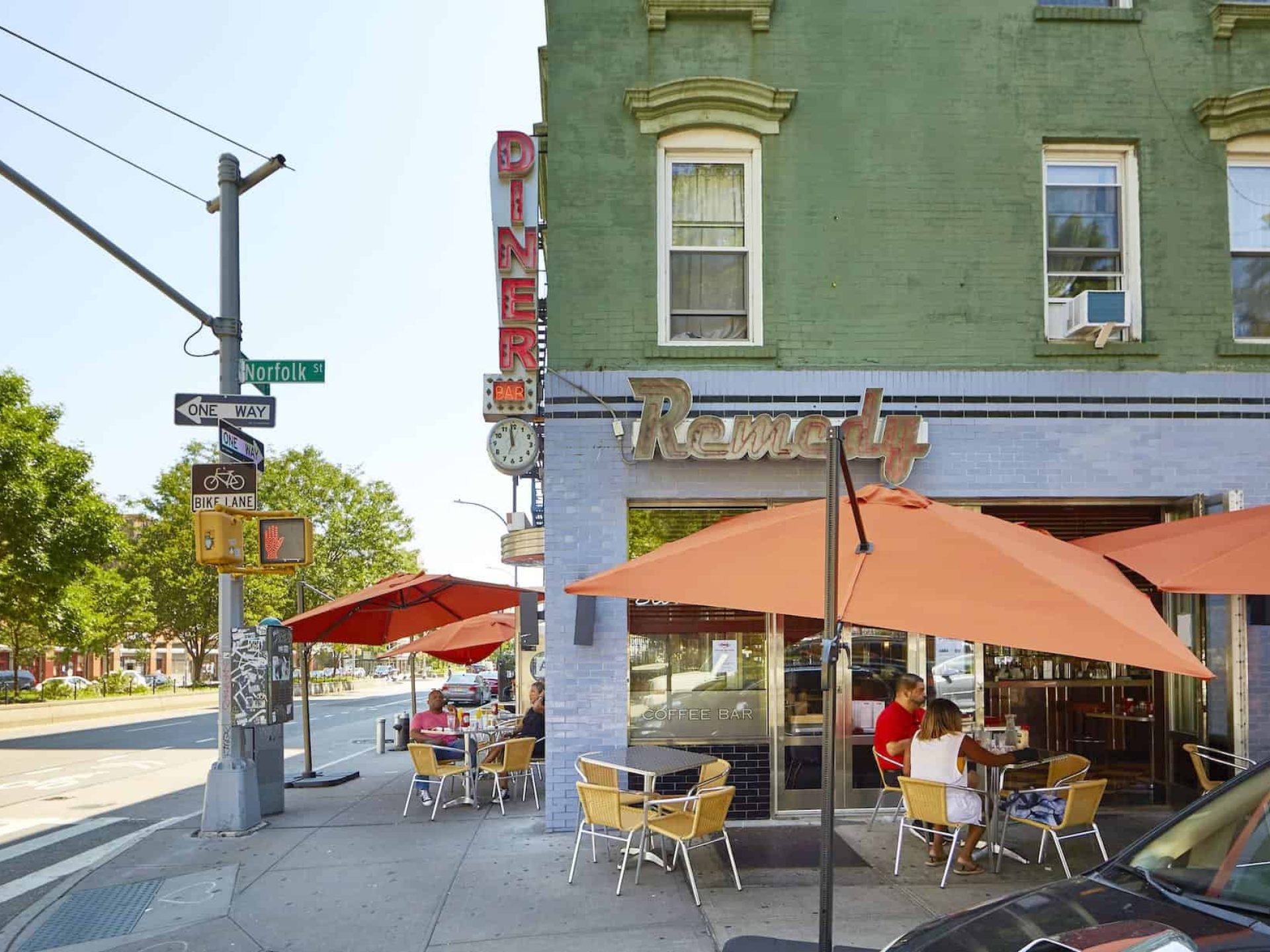 Exterior of Remedy Diner on Norfolk St in New York with lit "Diner" sign and outdoor seating and large red umbrellas.