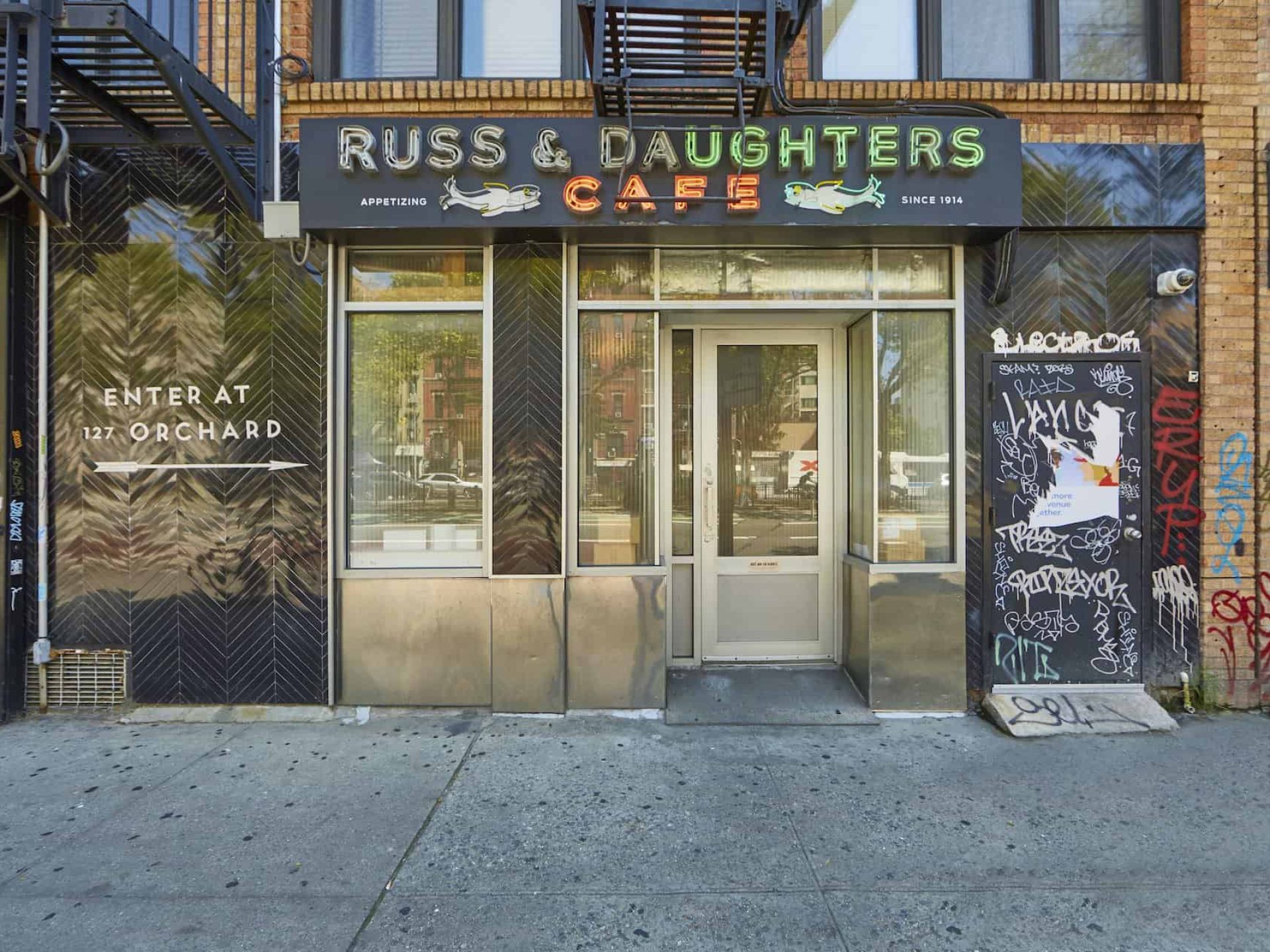 Entrance to Russ & Daughters Cafe in New York. Neon sign above building door, large windows and metal paneling.