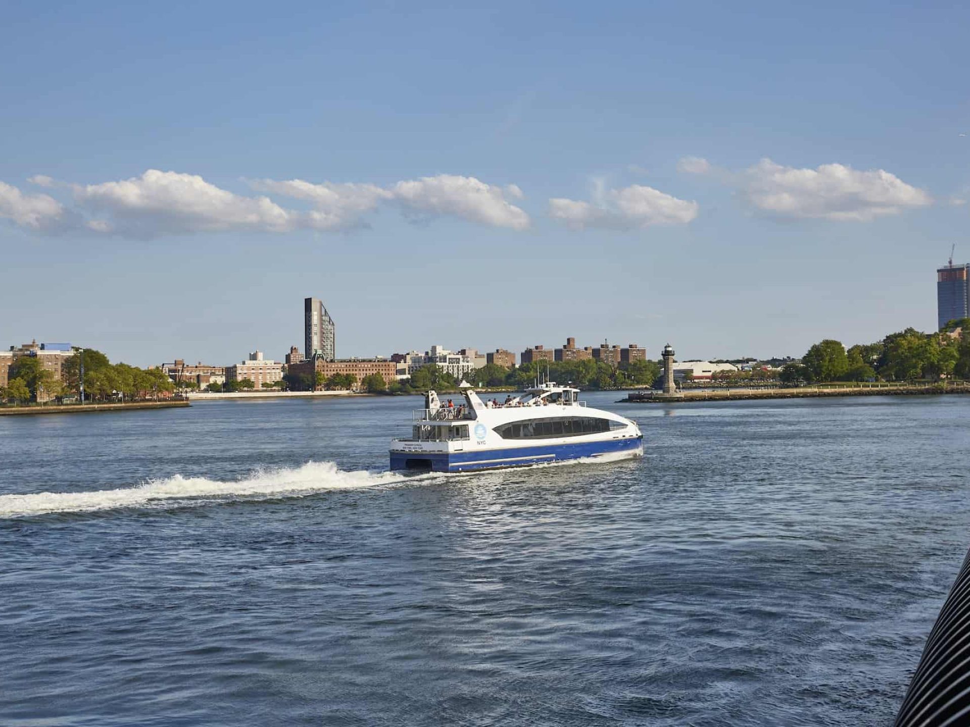 New York City ferry on the East River. White and blue ferry boat with passengers and city buildings in the background.