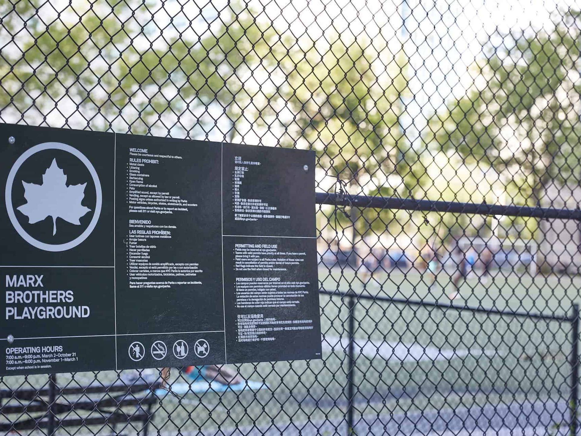 Close up of Marx Brothers Playground park sign. Green sign with white text and images mounted on a wire fence.