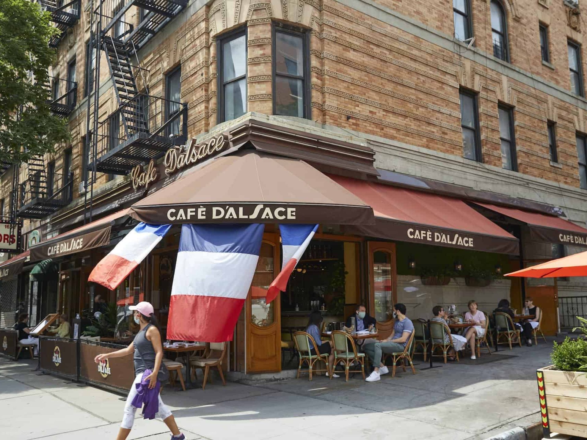 Exterior of the restaurant Cafe Dalsace with a red awning, outdoor seating and french flags hanging from the awning.