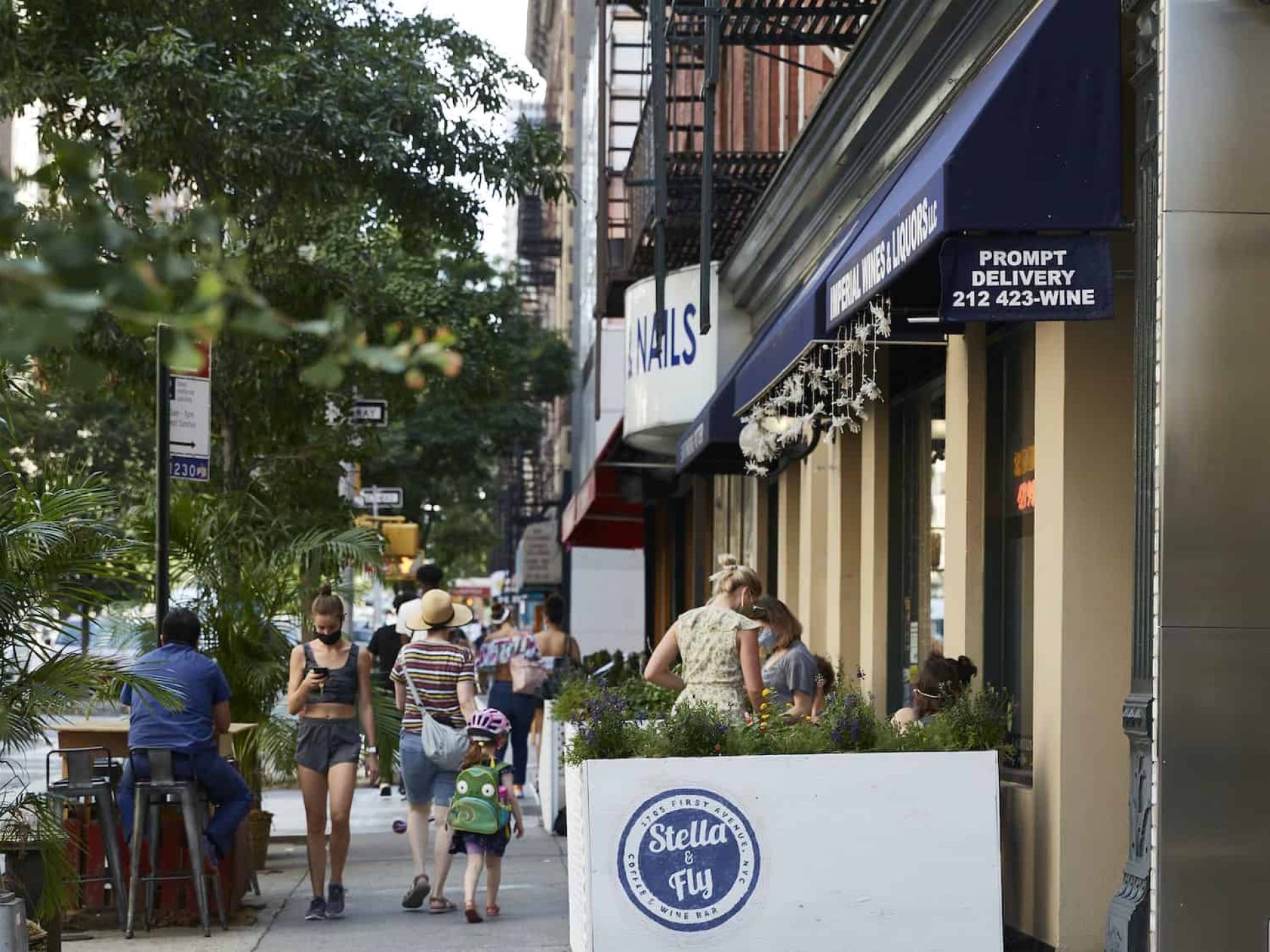 Exterior of the restaurant Stella & Fly in New York with a blue awning, outdoor seating and people walking on the sidewalk.