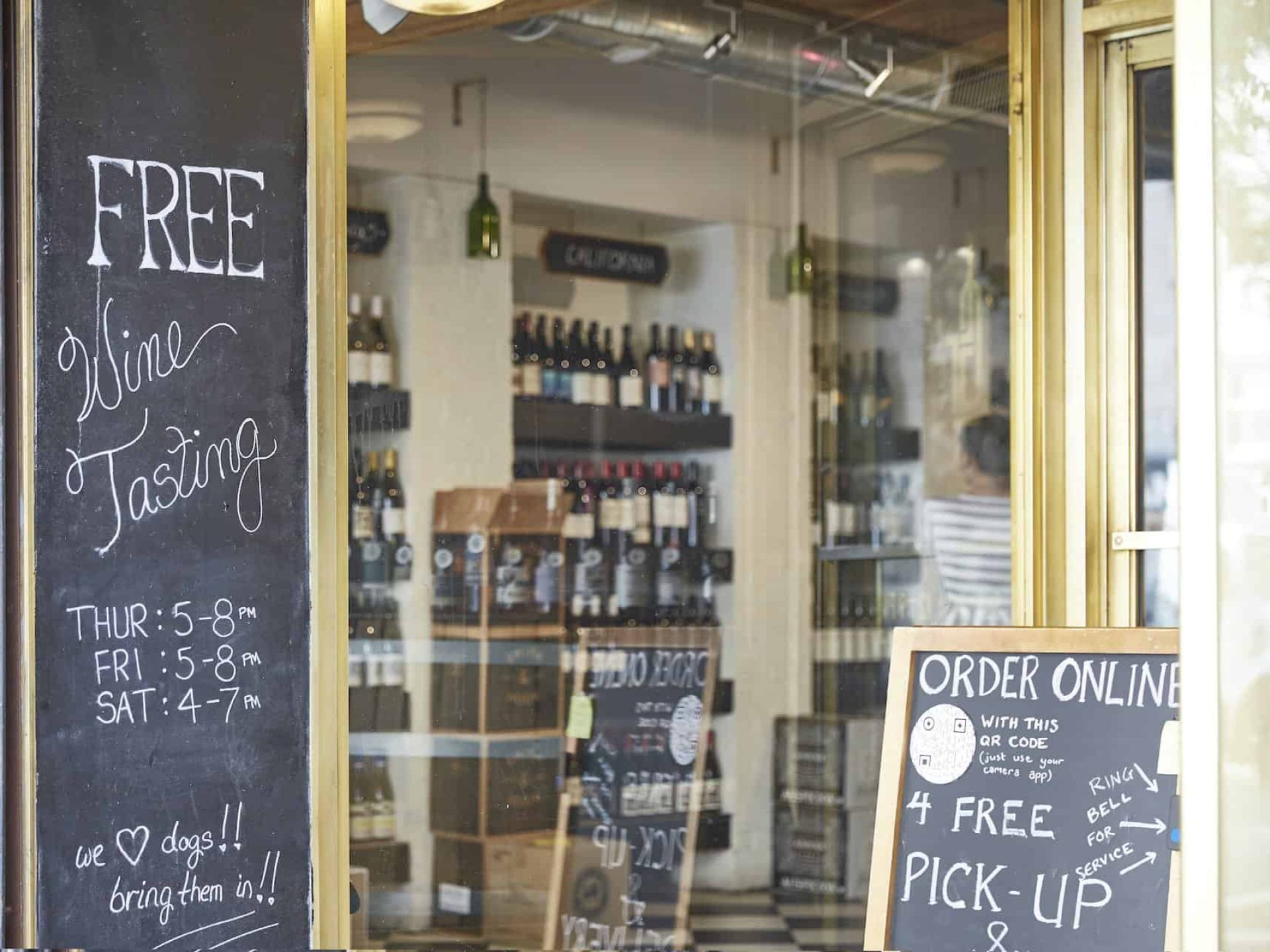 Close up of entrance to a wine shop in New York. Large windows with chalkboard signs promoting wine tasting times.