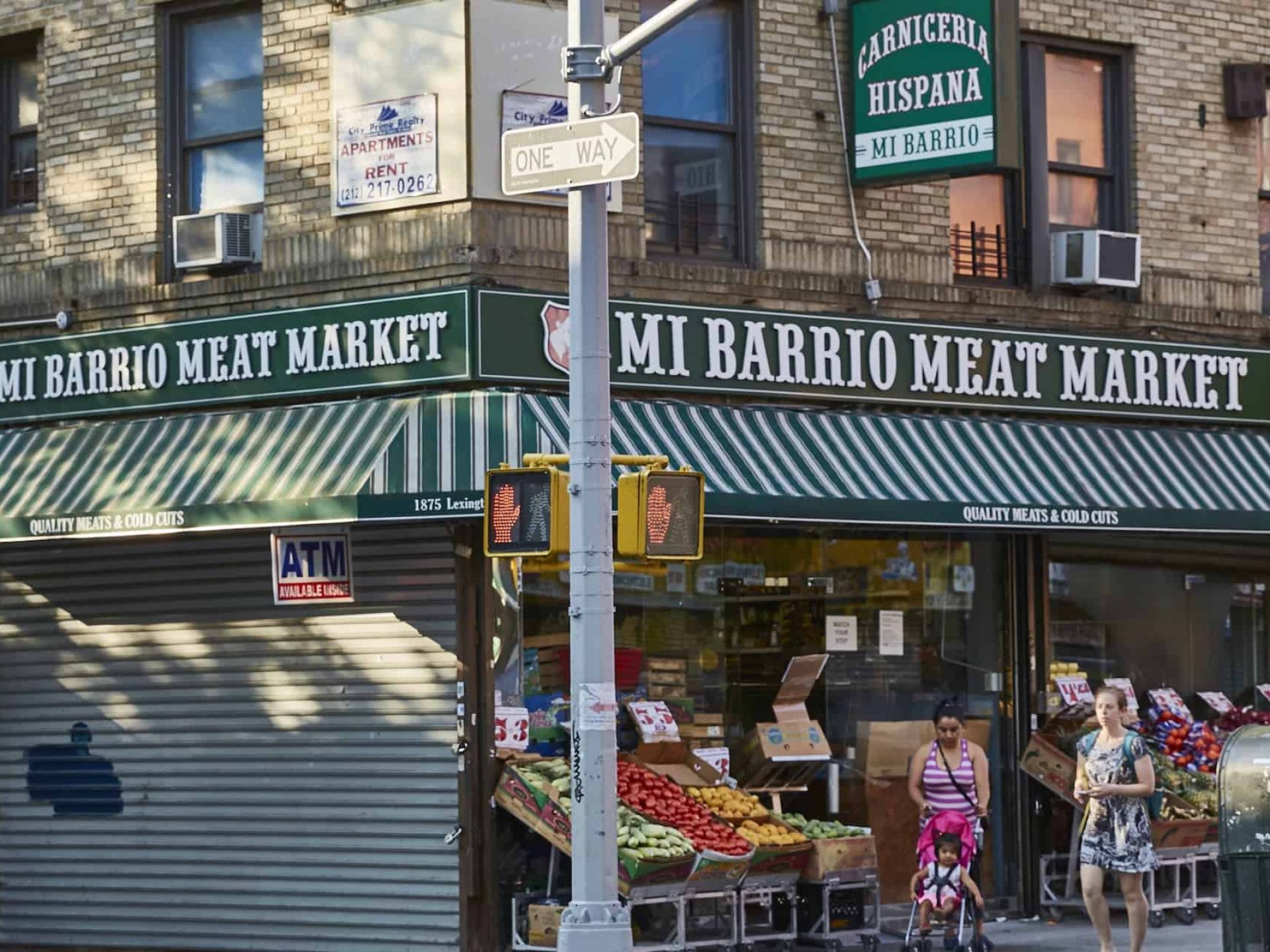 Exterior view of Mi Barrio Meat Market in East Harlem. Brick building with large windows, metal security door and an awning.