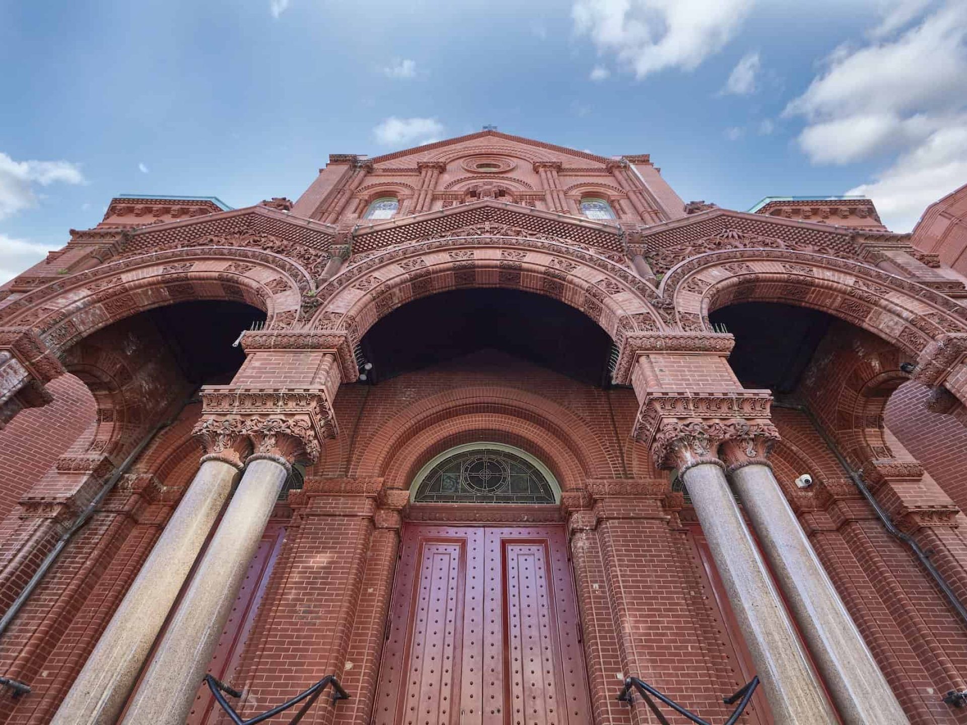 Close up of tall red brick building in New York. Large red double doors, stone columns supporting arched entryway.