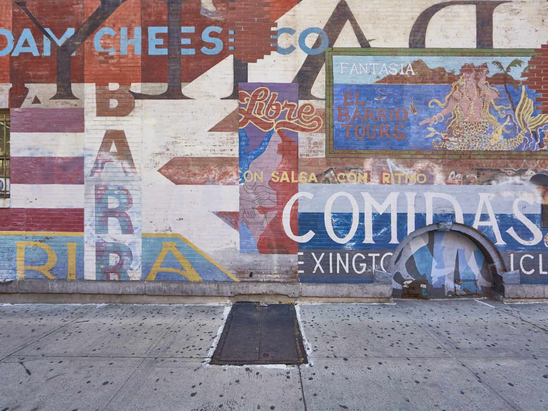 Brick wall in East Harlem, New York with street art containing business names, national flags, and Spanish words.