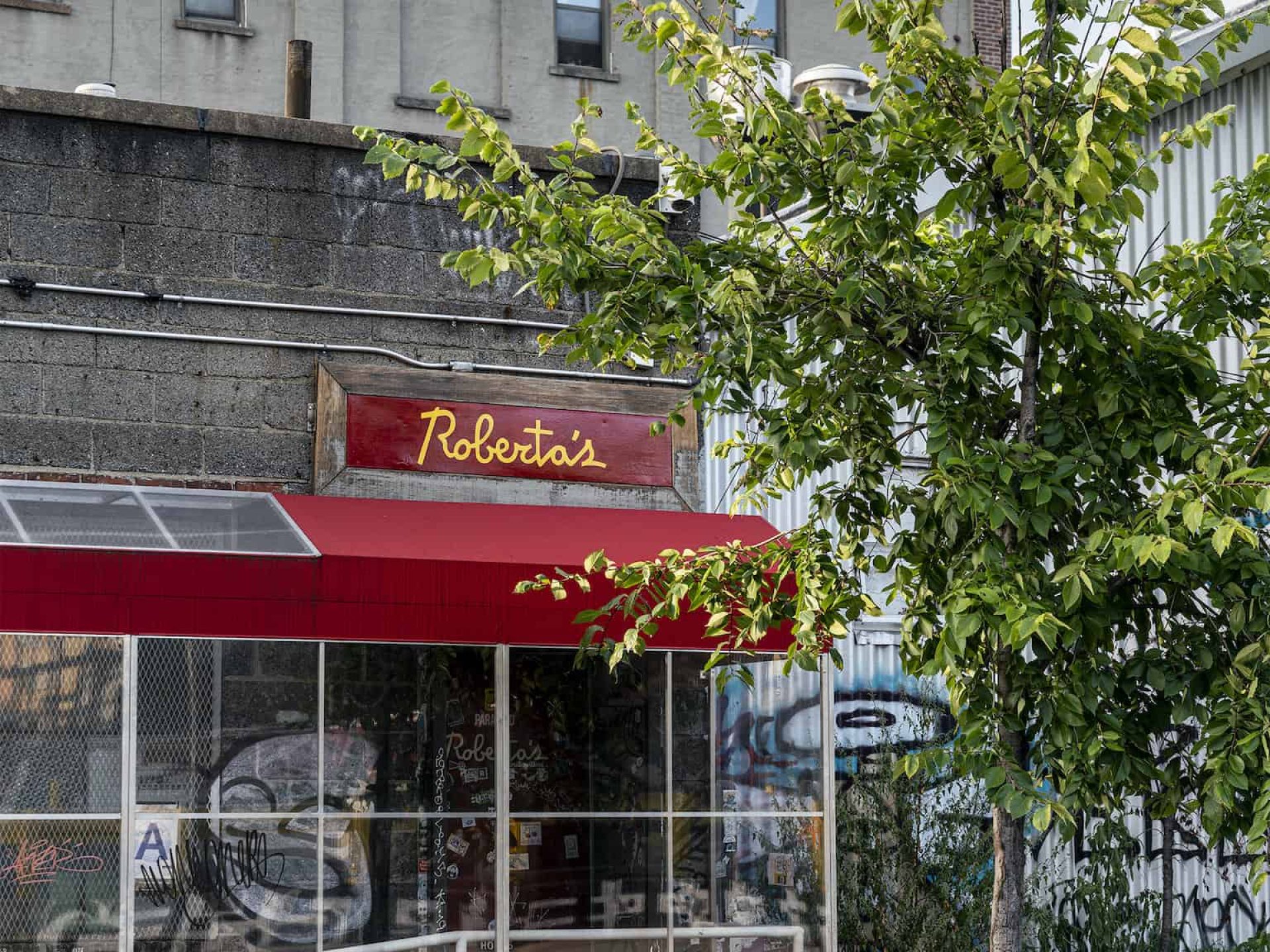 Exterior of Roberta's restaurant with covered entry with red awning and red sign with company name in yellow letters.