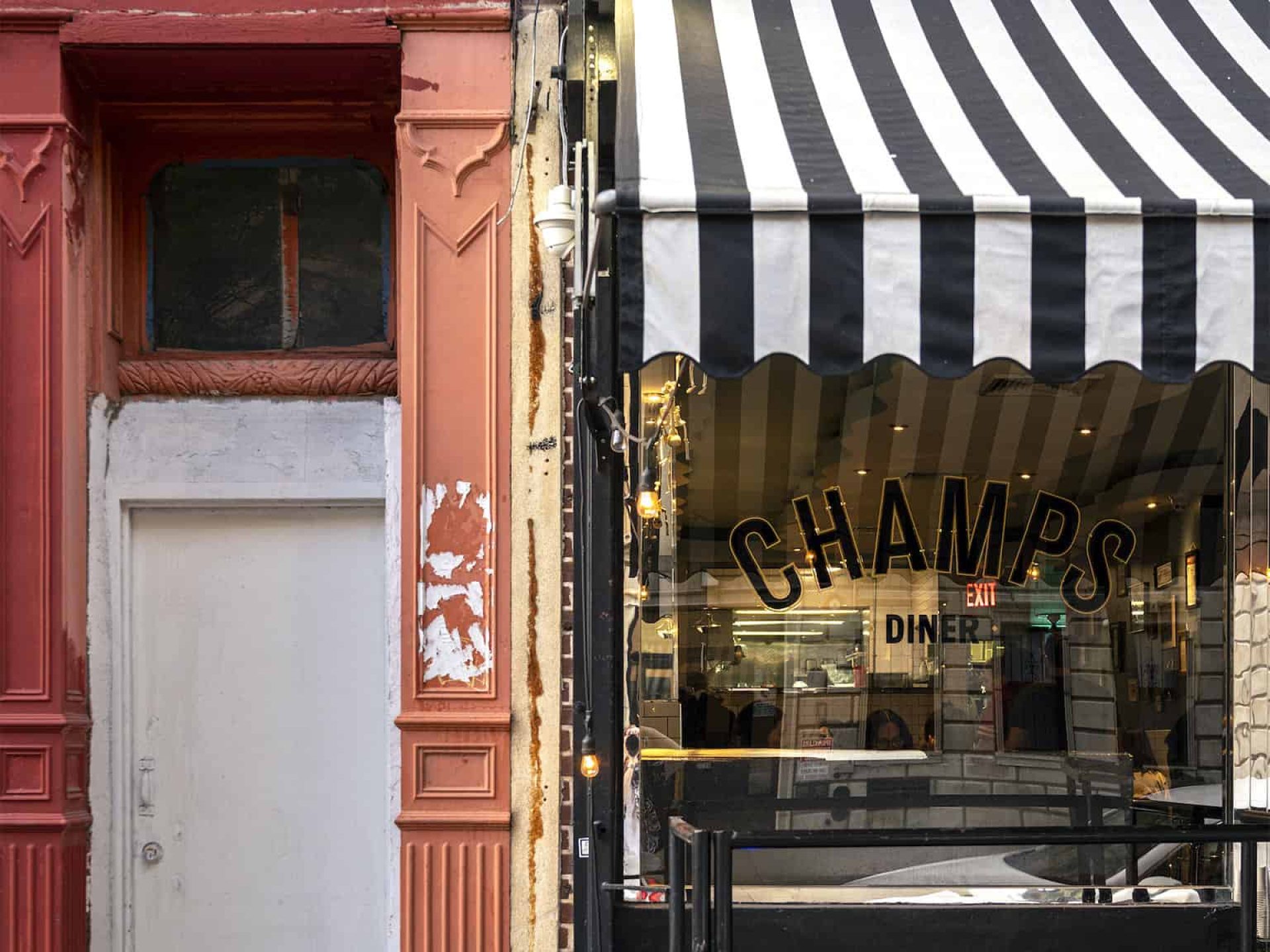 Close up of Champs Diner in the Williamsburg neighborhood. Large window with diner name and striped awning over the entrance.