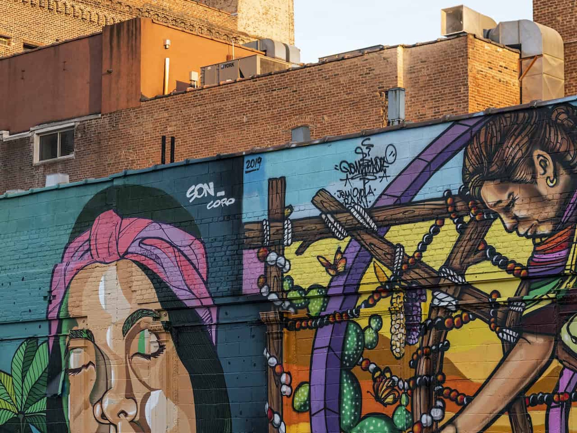 Street view of a painted brick wall with two images including one with a person with a headband, dark hair & green lipstick.