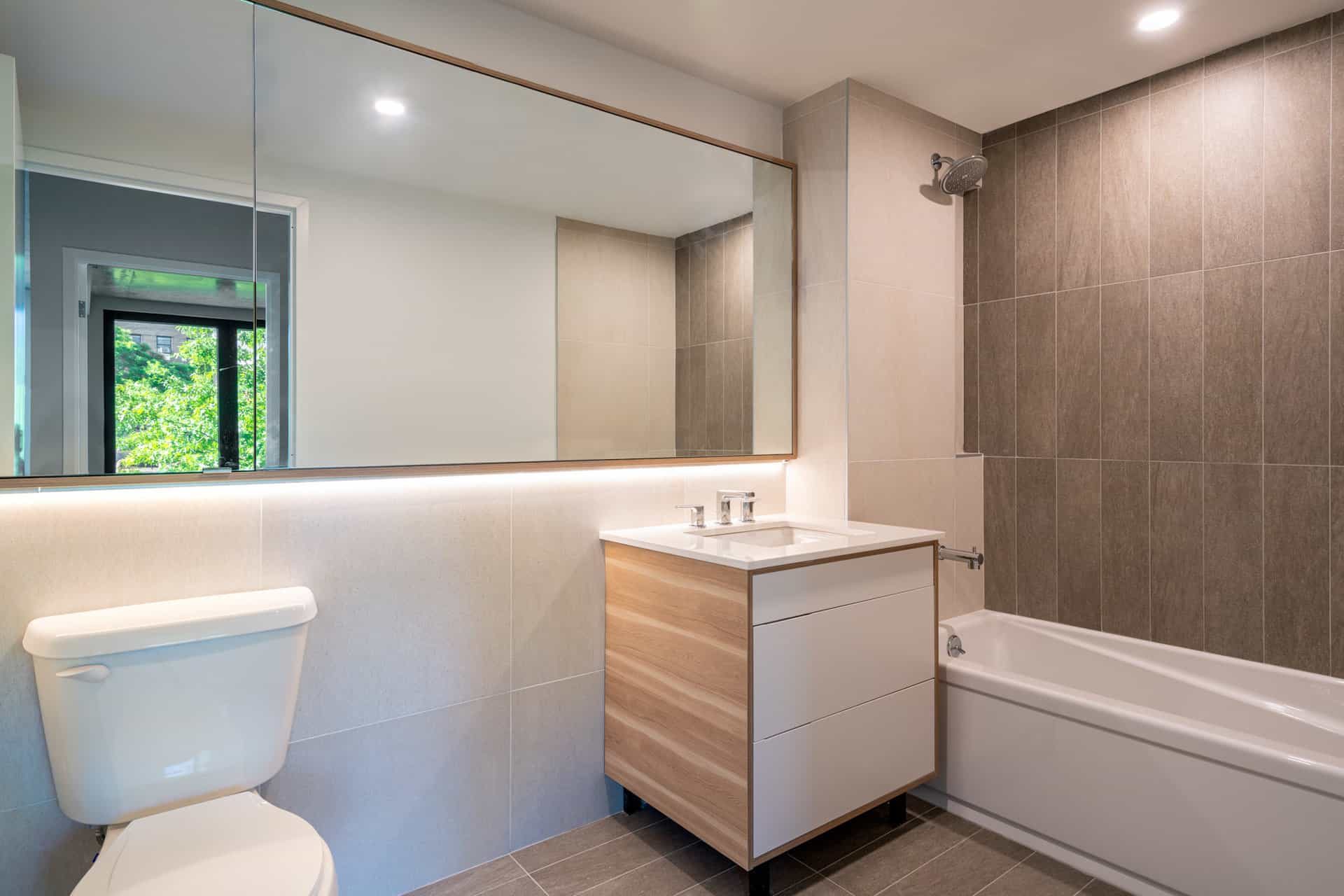 Bathroom at 222 Johnson Avenue apartments with a single vanity, large mirror, tile walls and a soaking tub with shower.