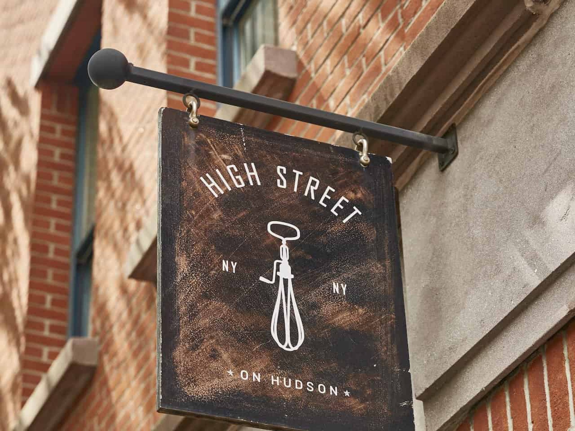 Close up of a hanging sign for High Street on Hudson restaurant in New York. Wood sign hanging from a metal post.