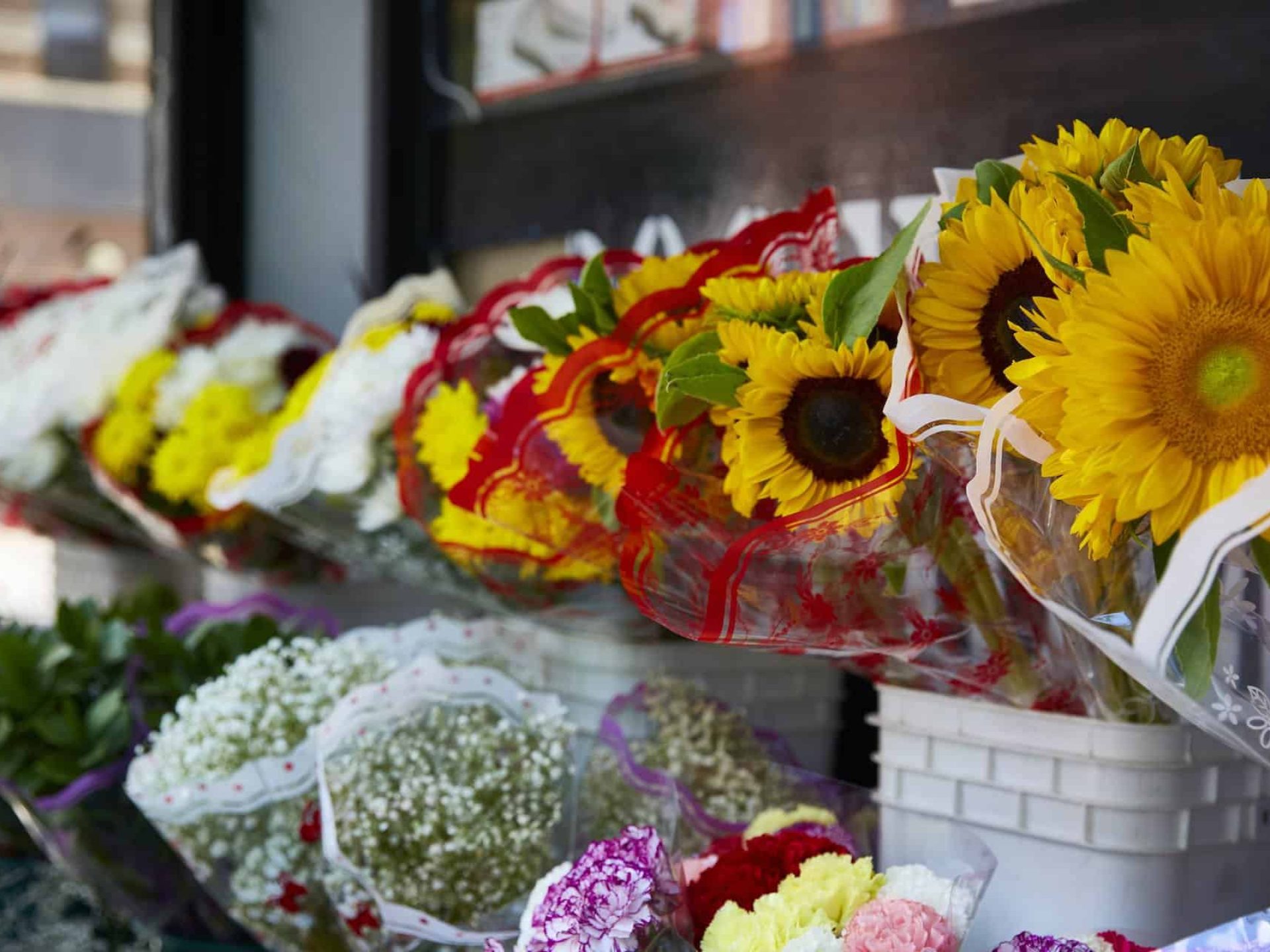 Close up of flowers in a display stand out on the street. Bouquets of sunflowers, daisy's and peony's in white buckets.