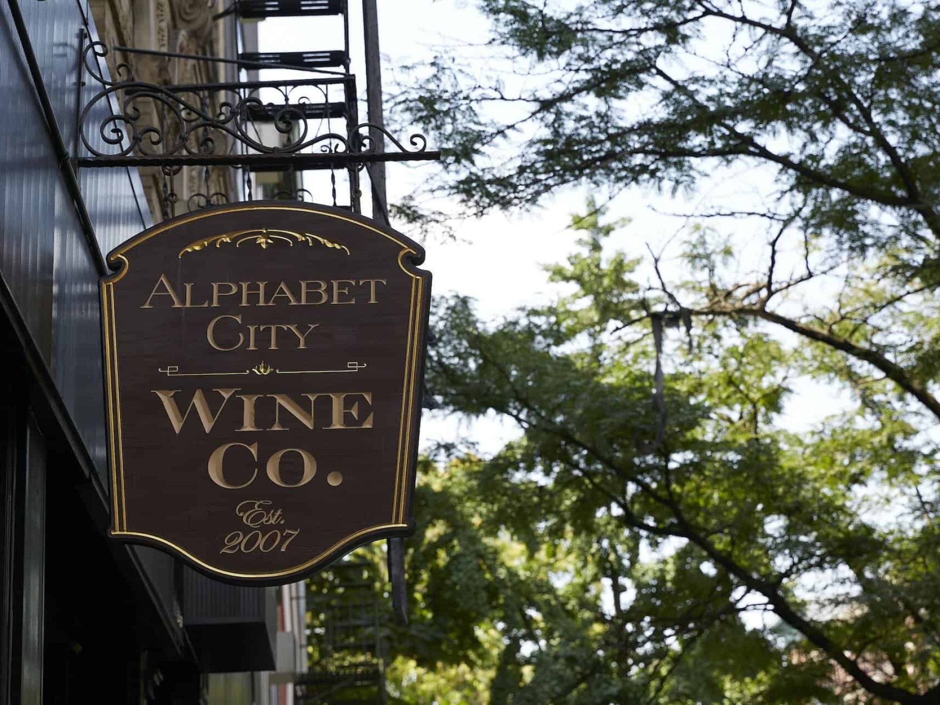 Close up of business sign for Alphabet City Wine Co. A brown sign with gold trim and lettering hanging above the entrance.