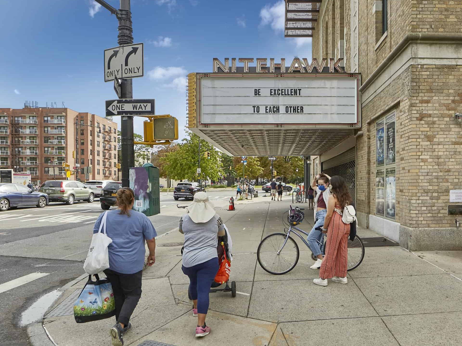 Street view of NiteHawk Cinema in Brooklyn, NY. Pedestrians walking on the sidewalk below a theater sign.