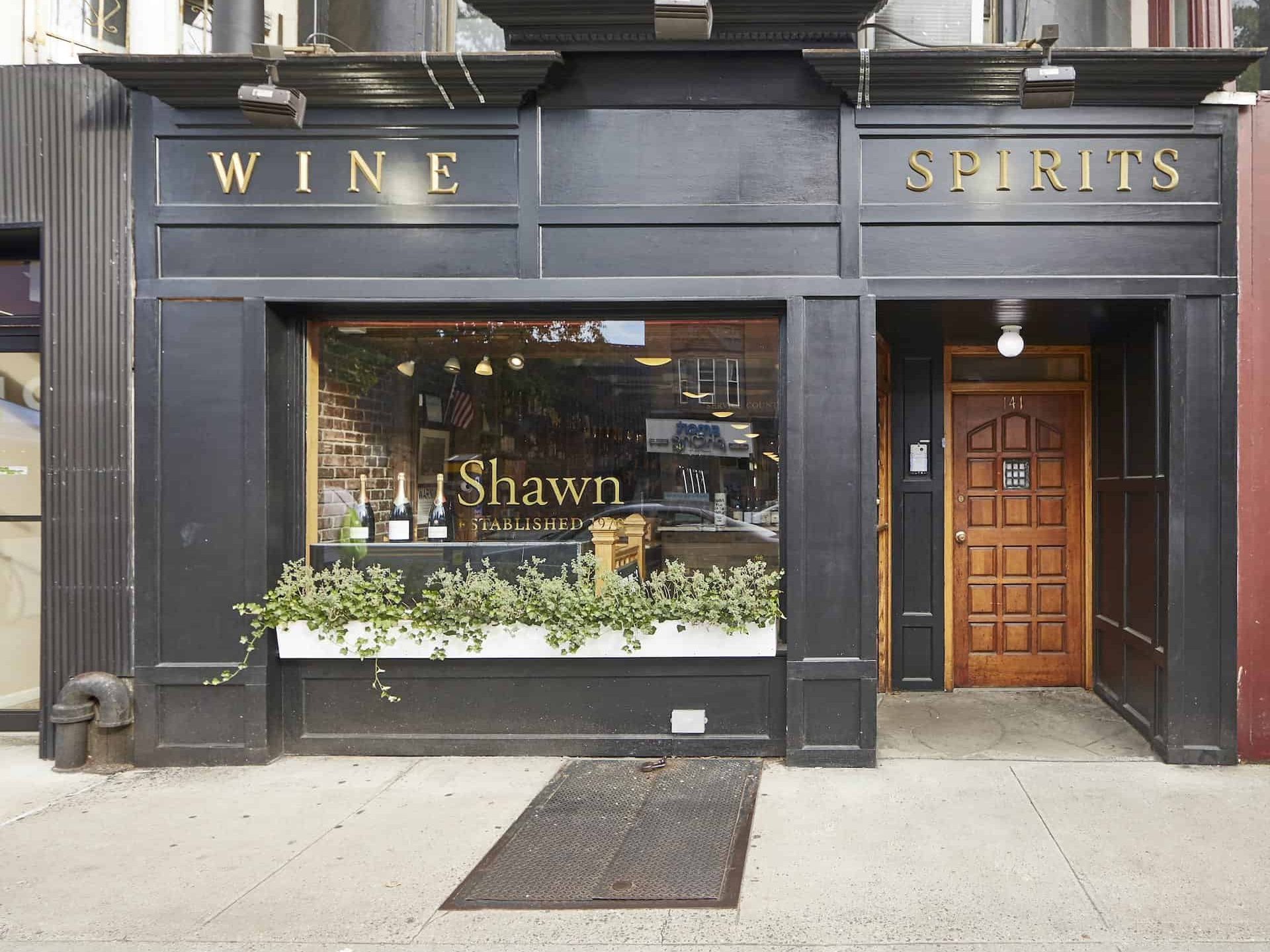 Storefront of Shawn Wine and Spirits in Brooklyn. Black wood exterior with gold letters, a large window and wood door.