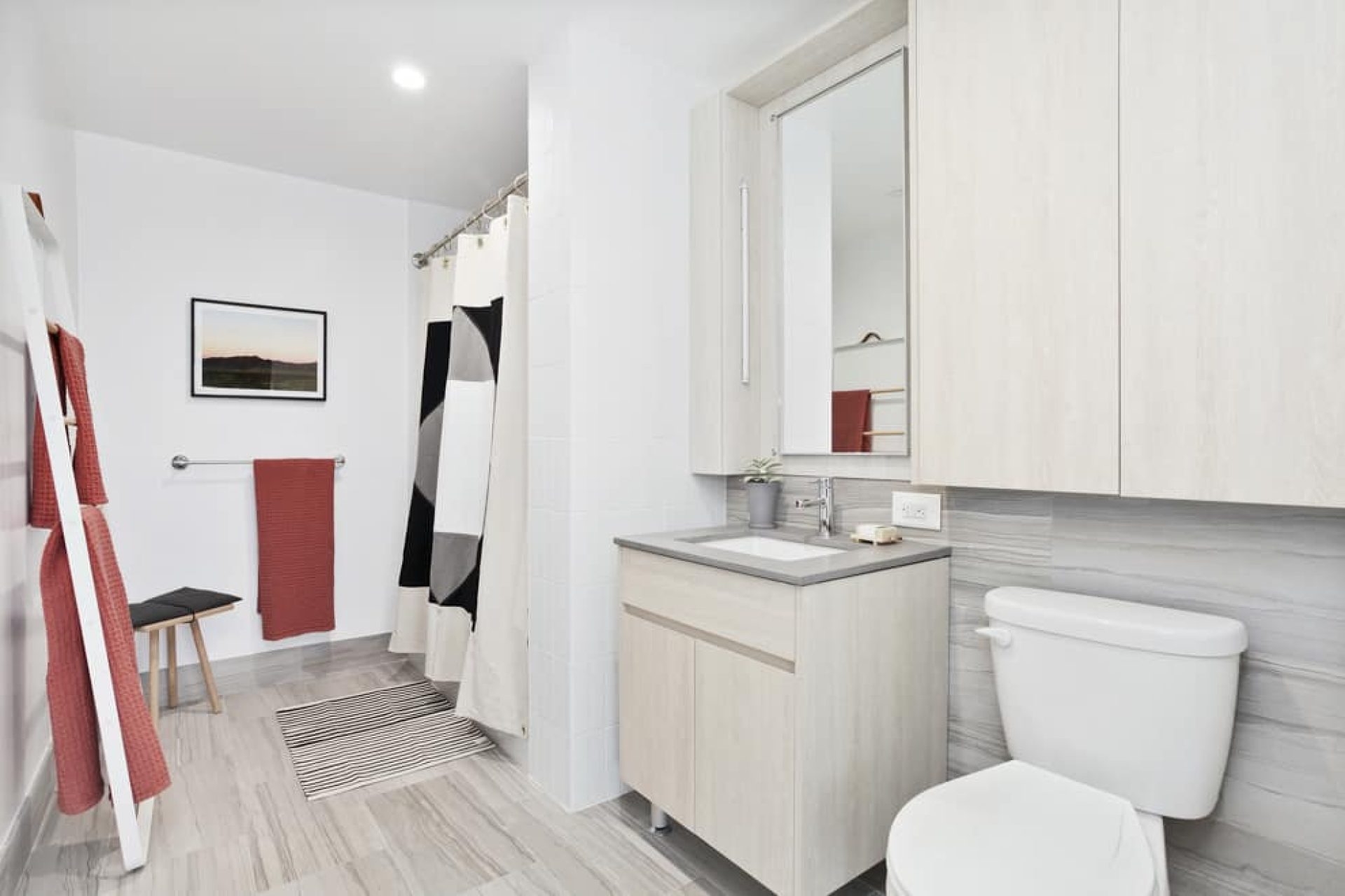 Bathroom at 66 Ainslie Street apartments with a single vanity, rectangle mirror, tile floors and soaking tub with shower.